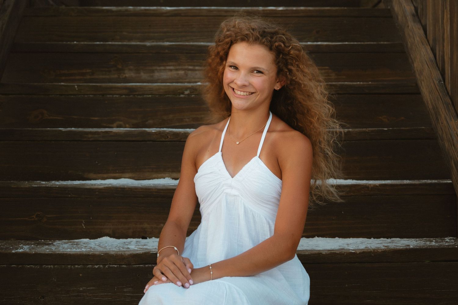 Woman in white dress sitting on wooden stairs with natural lighting.
