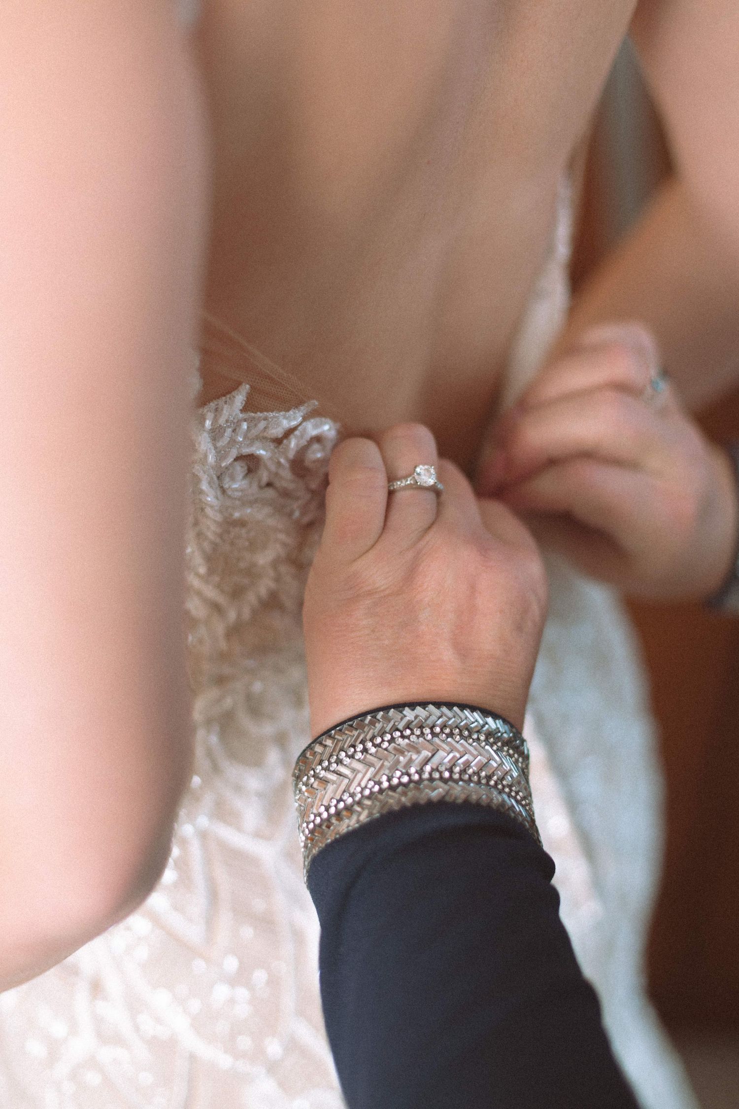 Close-up of hands fastening buttons on back of lace wedding dress before ceremony.