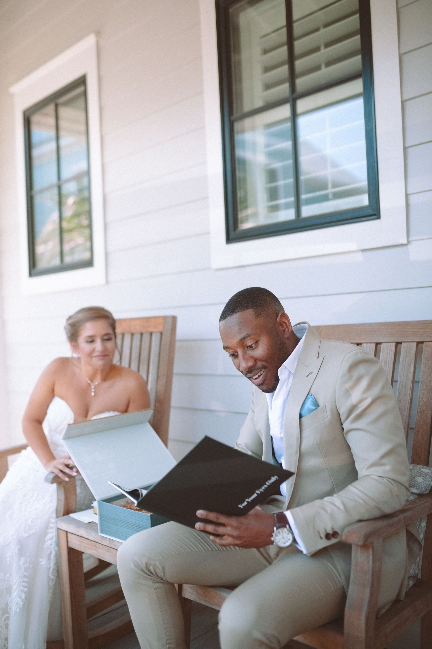 Bride and groom exchanging gifts on a sunny porch, groom reading from a black book.