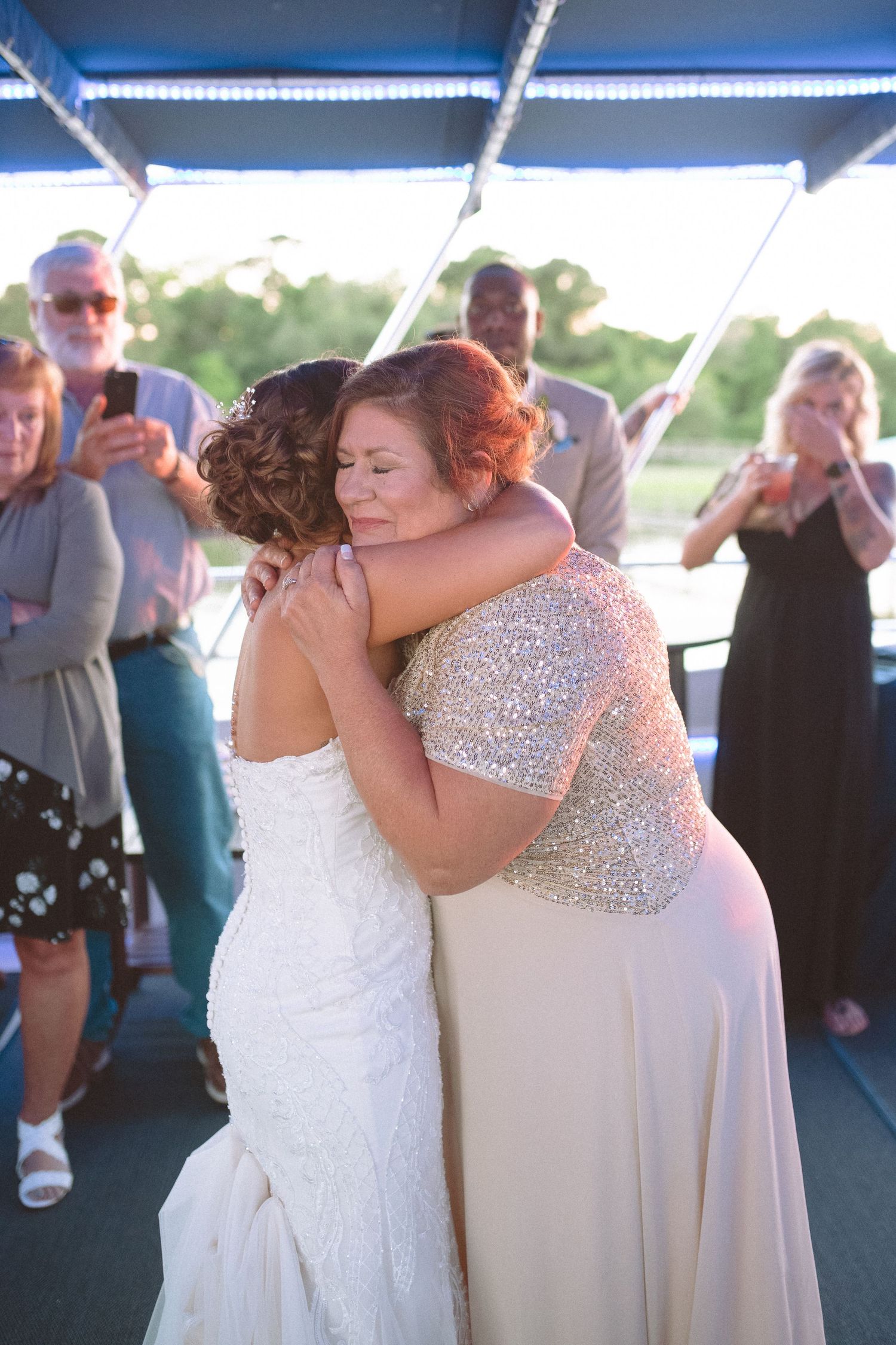 Bride and mother sharing an emotional hug during a wedding reception dance on a boat deck.