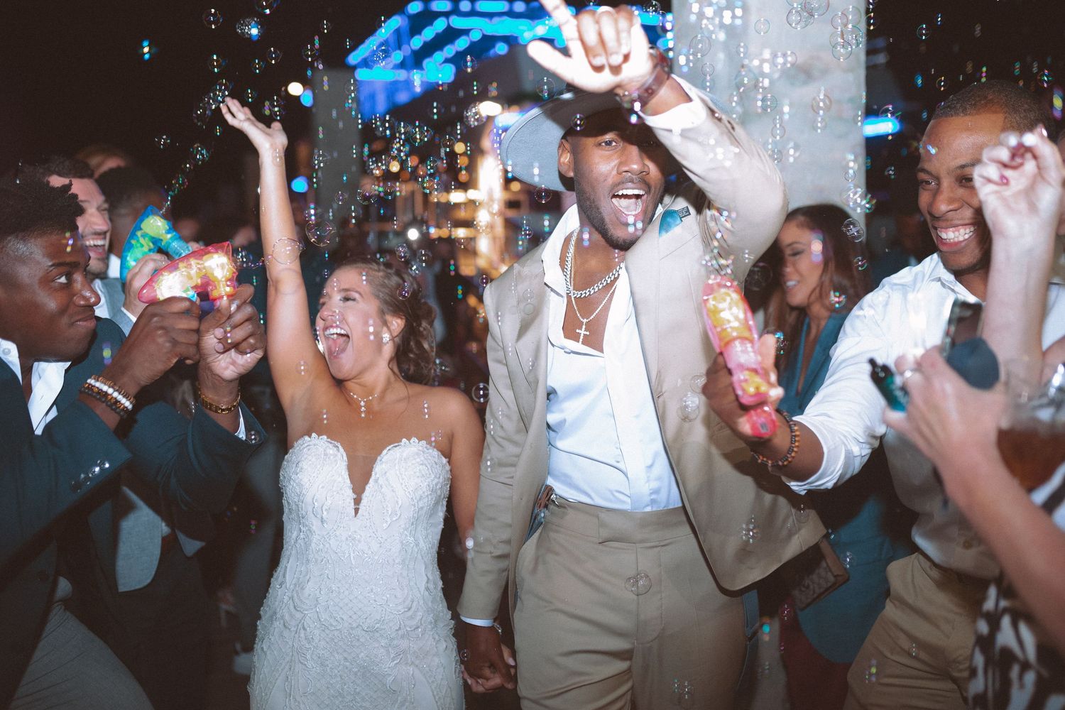 Bride and groom celebrate joyfully with guests at outdoor wedding reception night party with confetti.