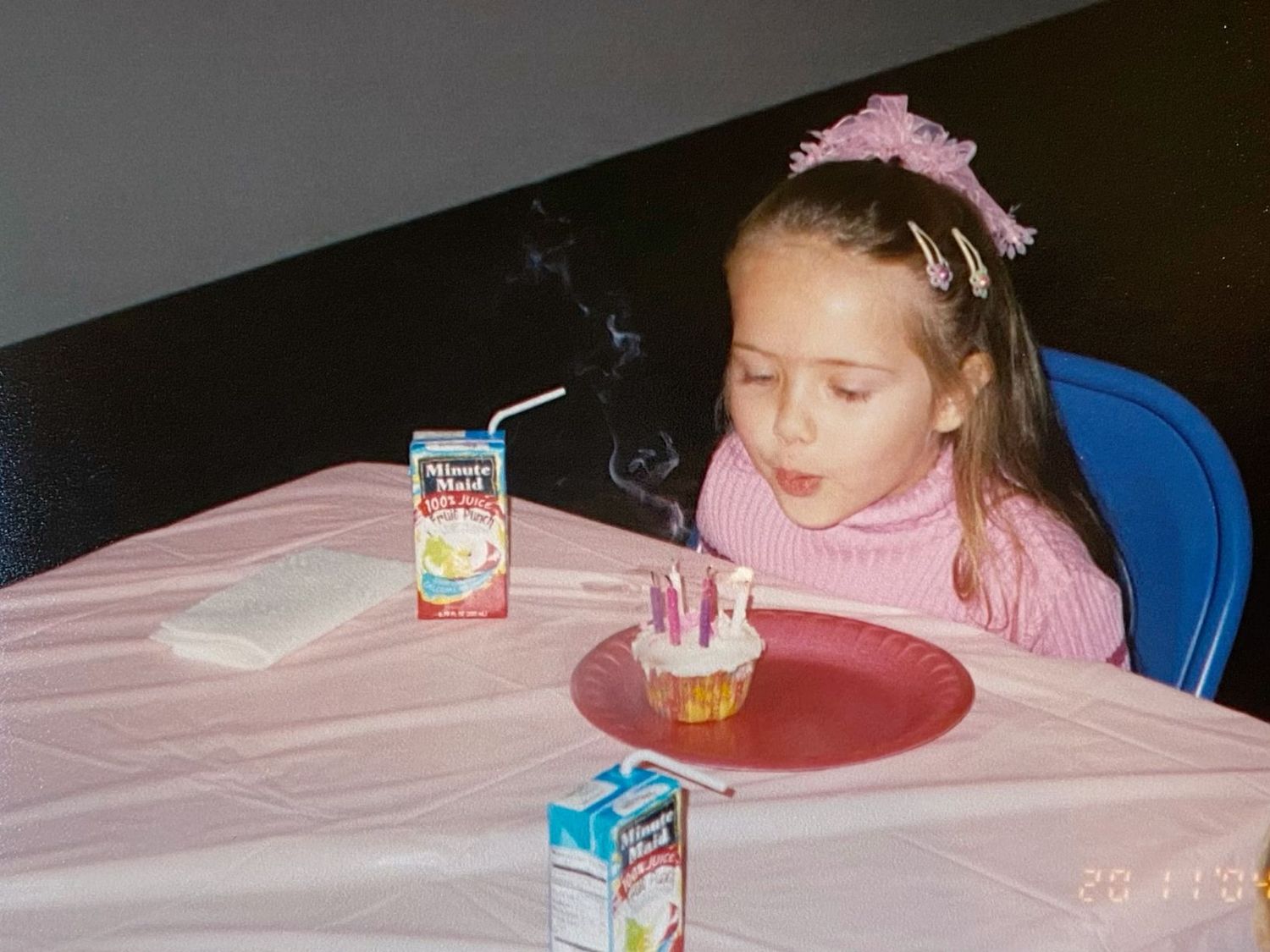 Young girl in pink blowing out birthday candles on a small cupcake at a table.