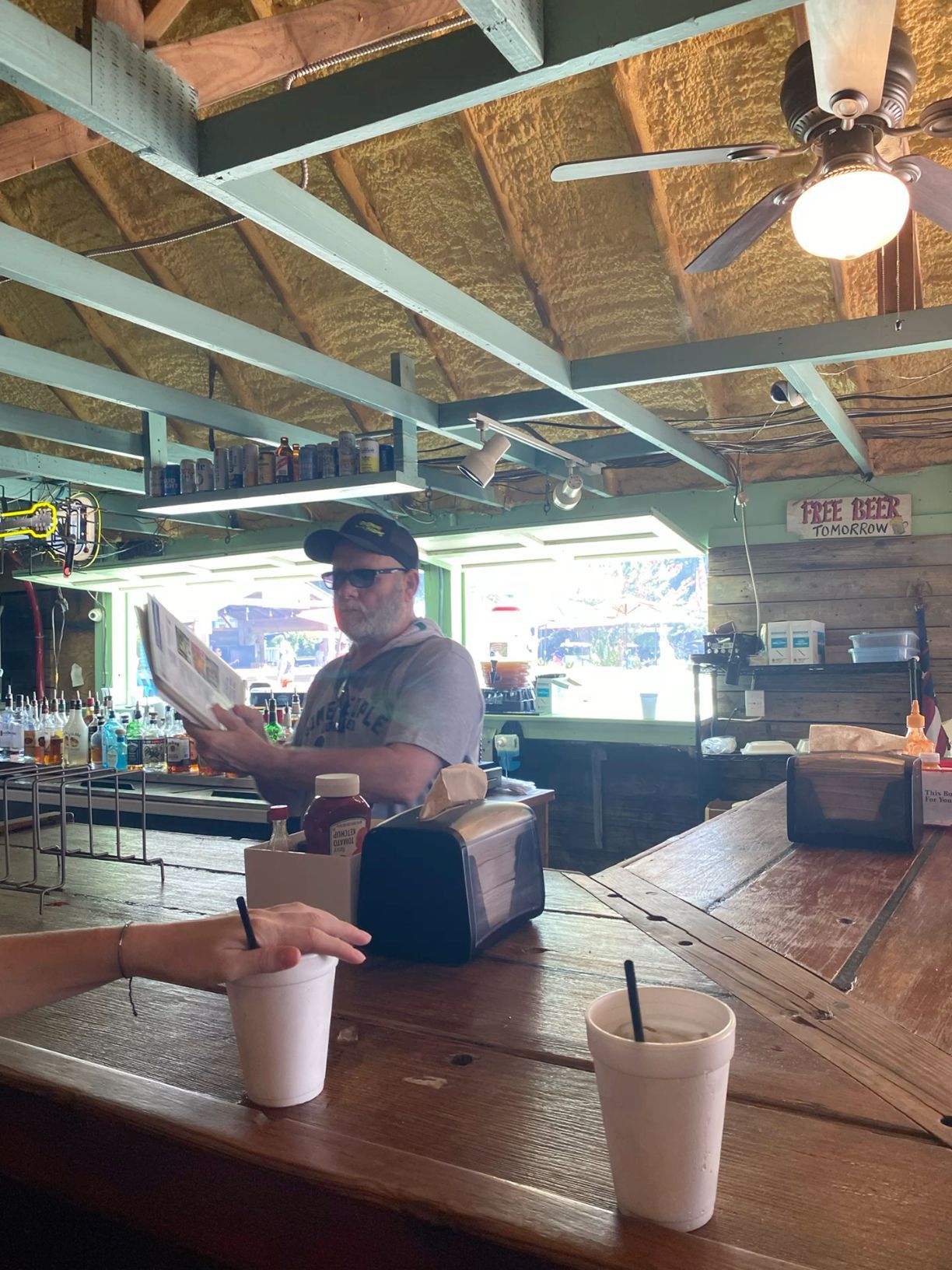 Casual rustic bar interior with wooden countertop, ceiling fan, and bartender reading menu.