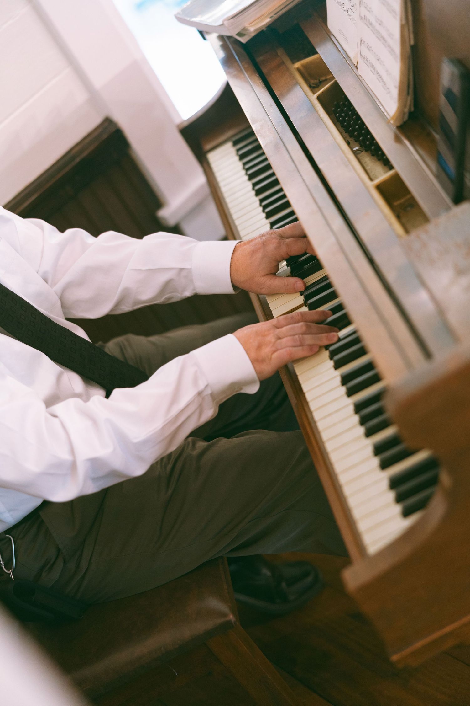 Man in white shirt playing an upright piano with sheet music, captured from above in warm tones.