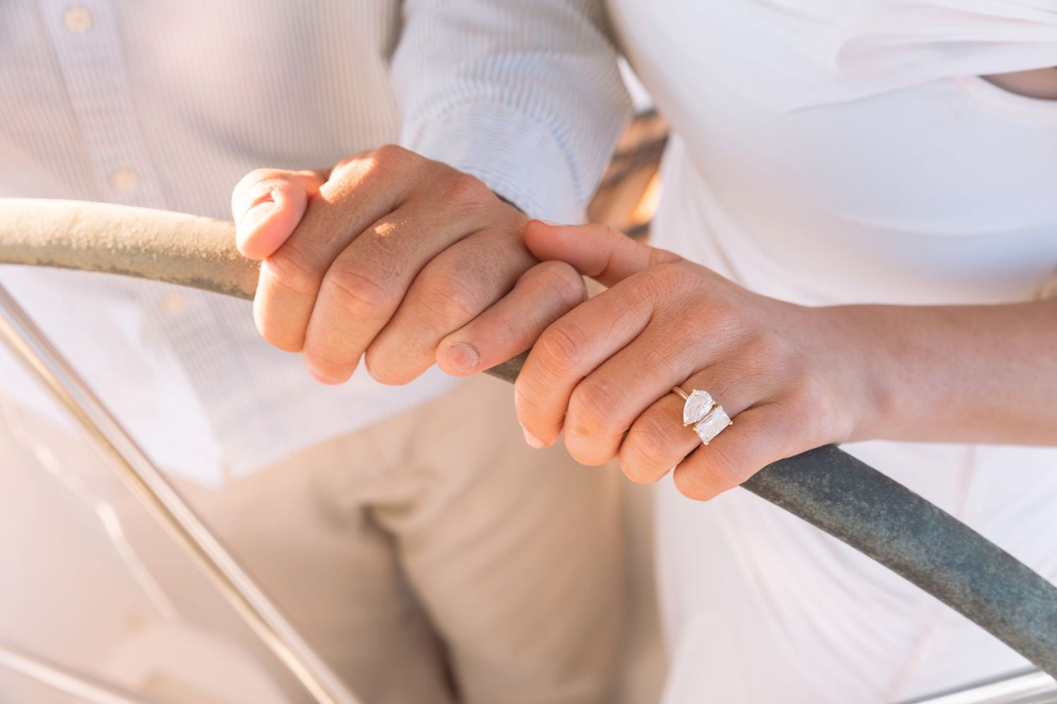 Close-up of a couple holding hands on a boat, woman wearing a diamond engagement ring.