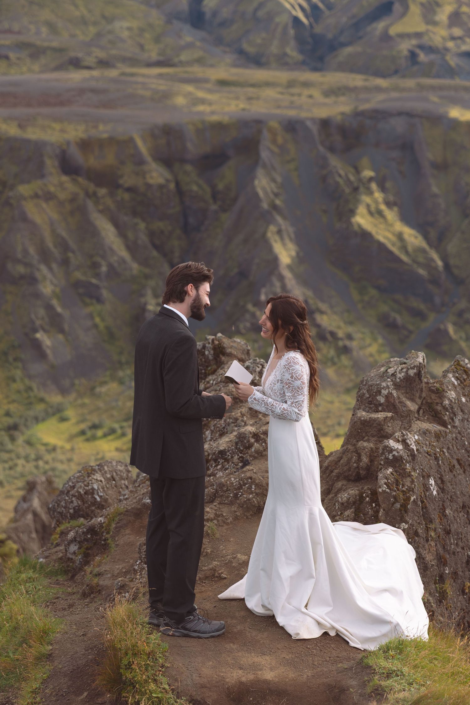 Groom reads handwritten vows to bride on scenic Iceland mountain overlook during outdoor elopement.