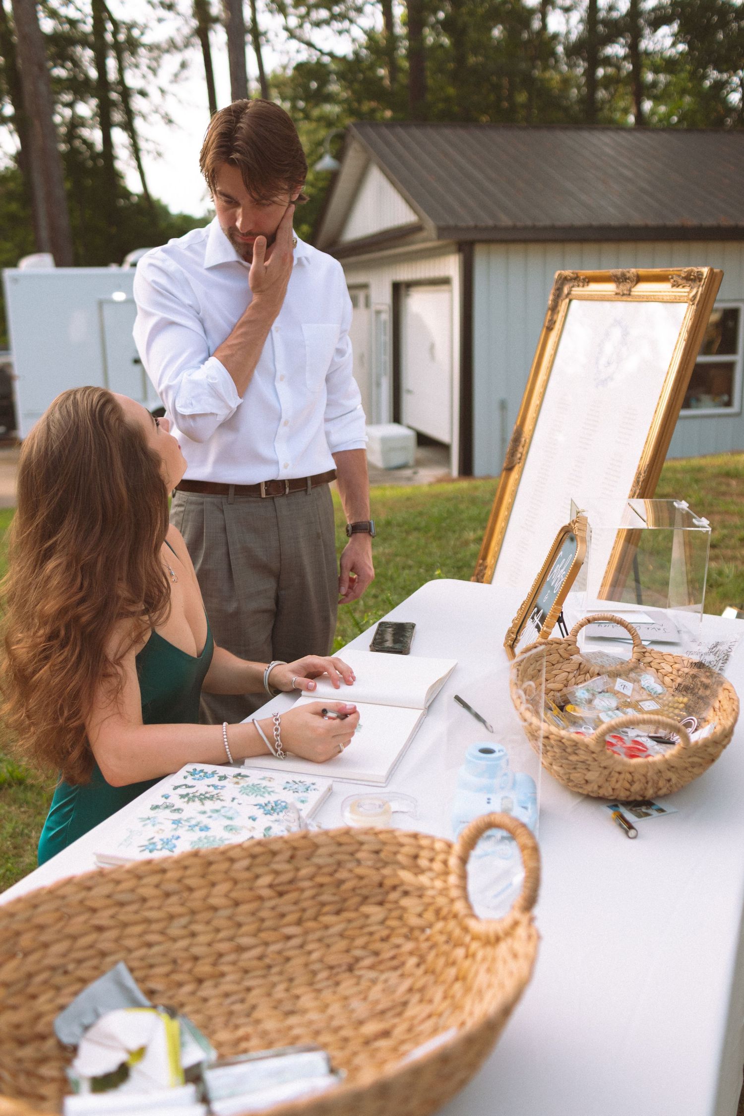 Guest signing wedding guestbook at an outdoor reception table with decorative baskets.