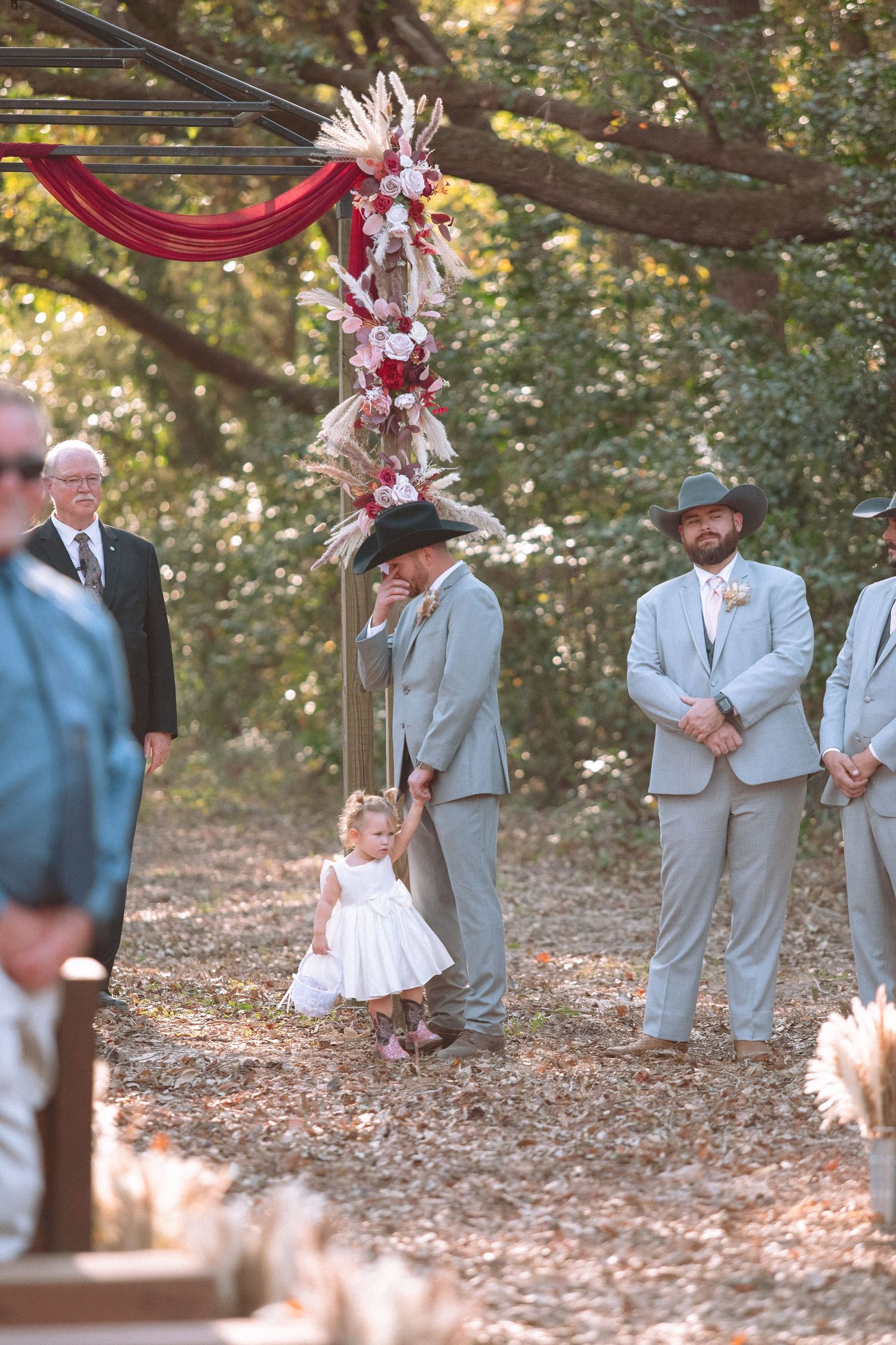 Emotional groom walks flower girl down the aisle at an outdoor woodland wedding ceremony.