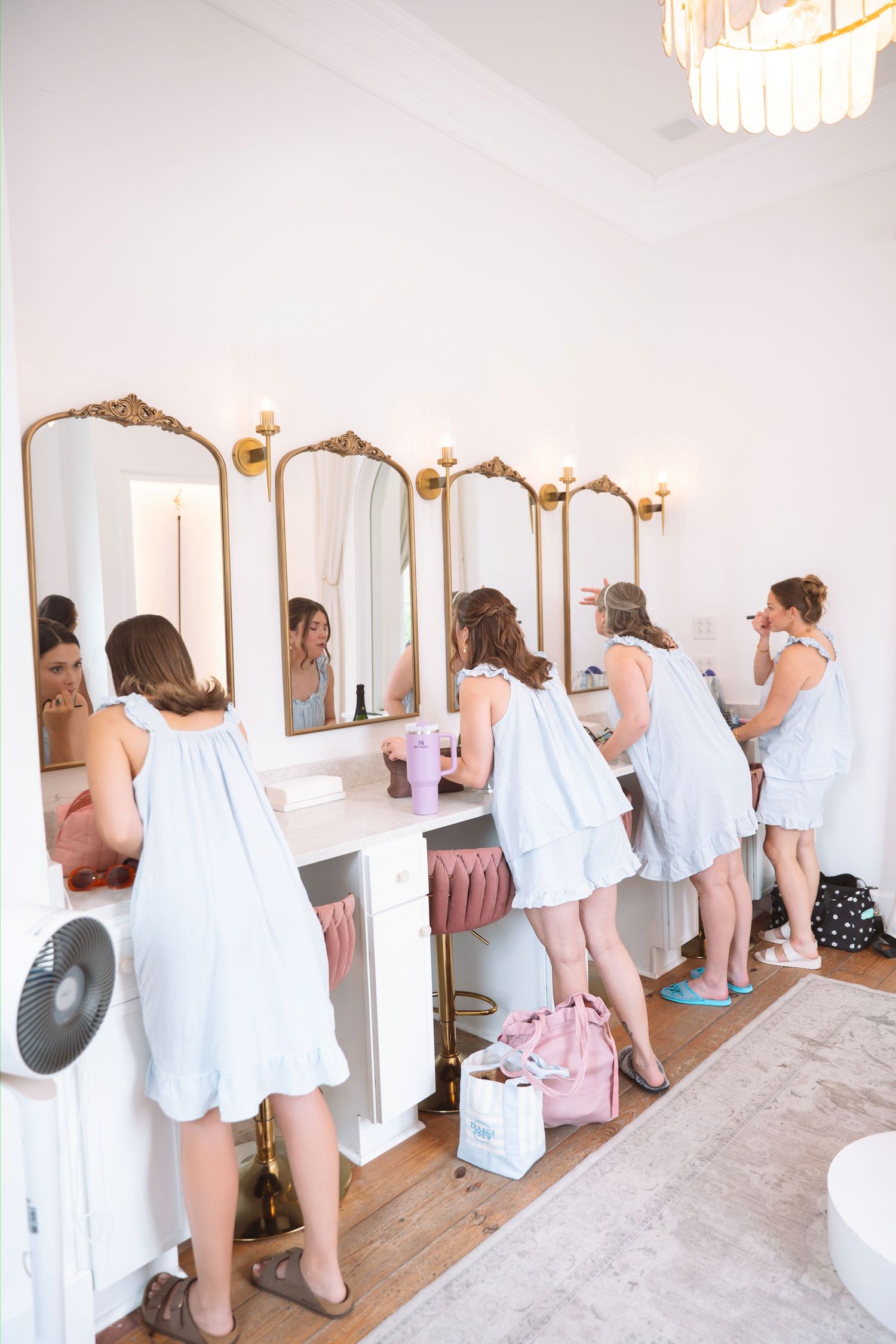 Bridesmaids in light blue robes getting ready at vanity mirrors in bright elegant bridal suite.