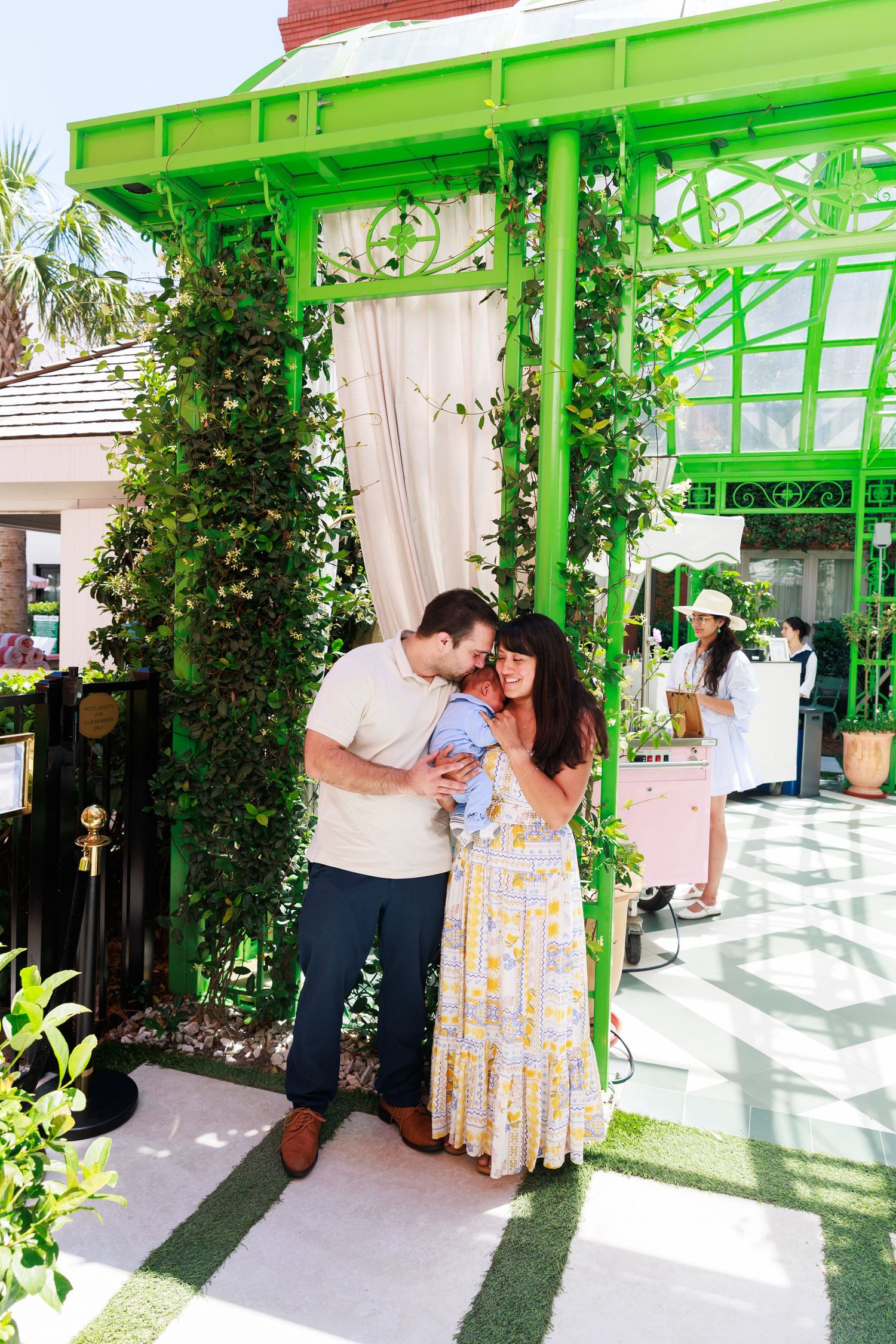 A couple shares a tender moment with their baby outside a green botanical gazebo covered in lush ivy.