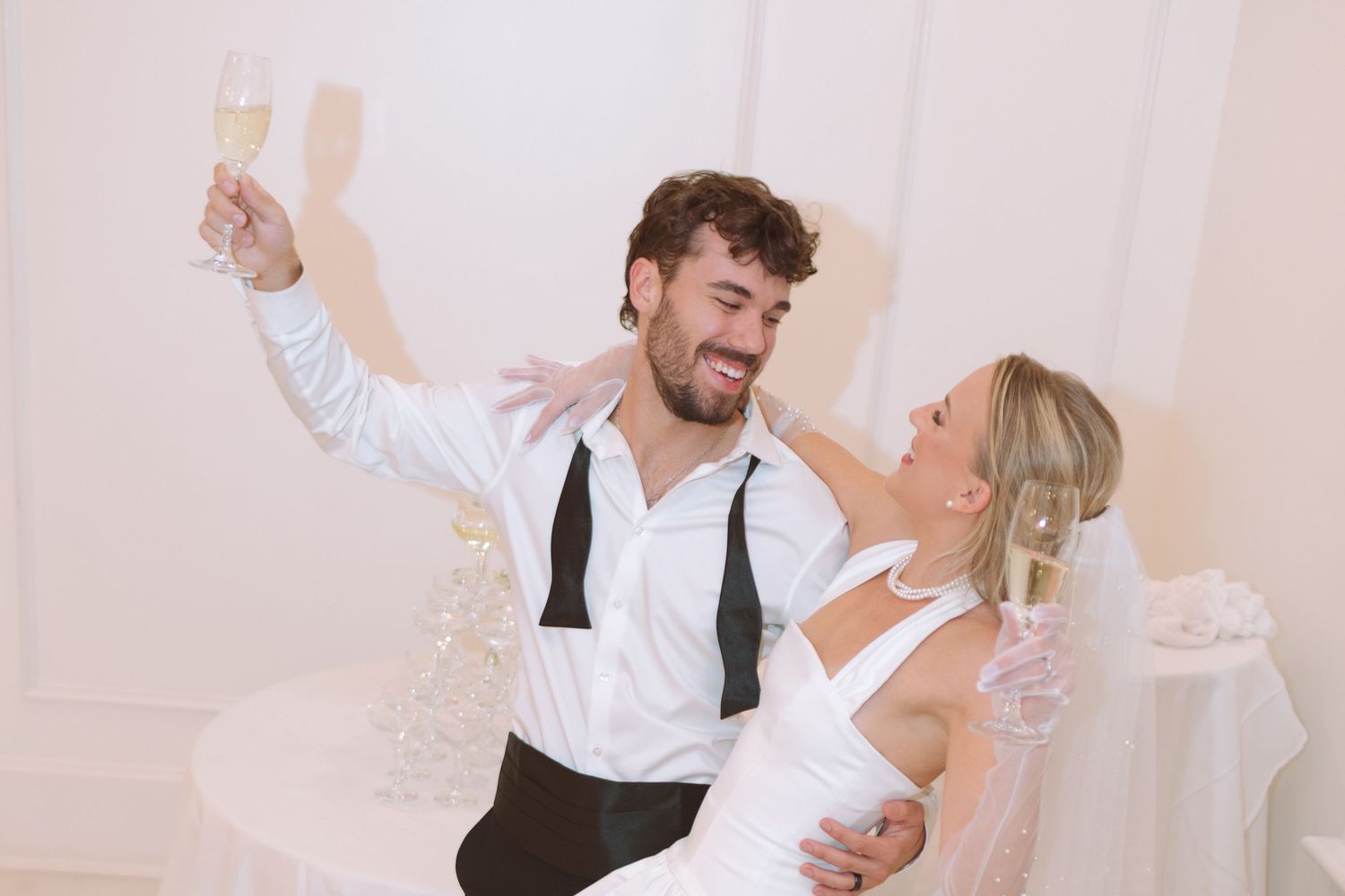 Joyful groom raising champagne glass with bride at wedding reception.