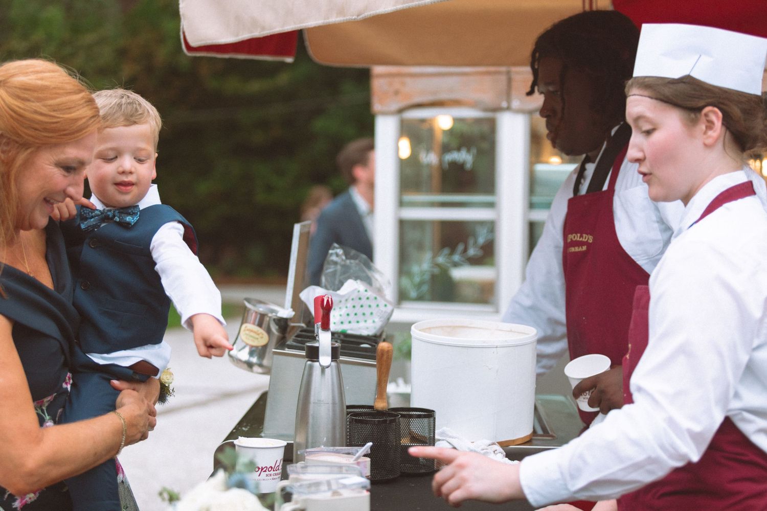 Wedding guests enjoy ice cream station served by staff in chef attire at outdoor reception.