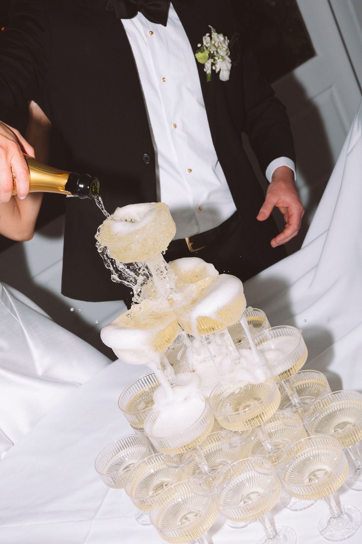 Groom pouring champagne into a tower of glasses at a wedding reception celebration.
