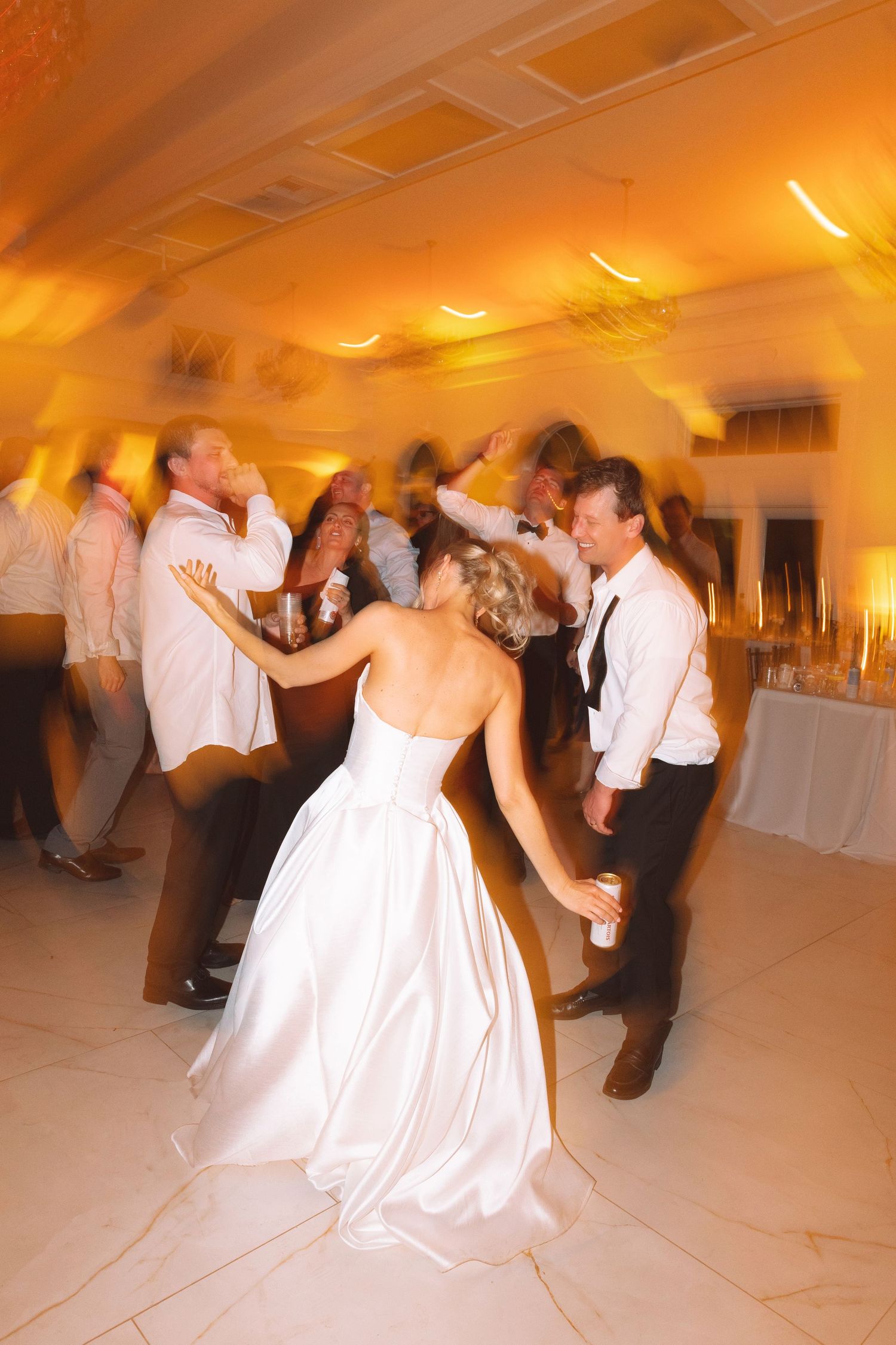 Bride in white gown dancing with groom and guests at a lively wedding reception.