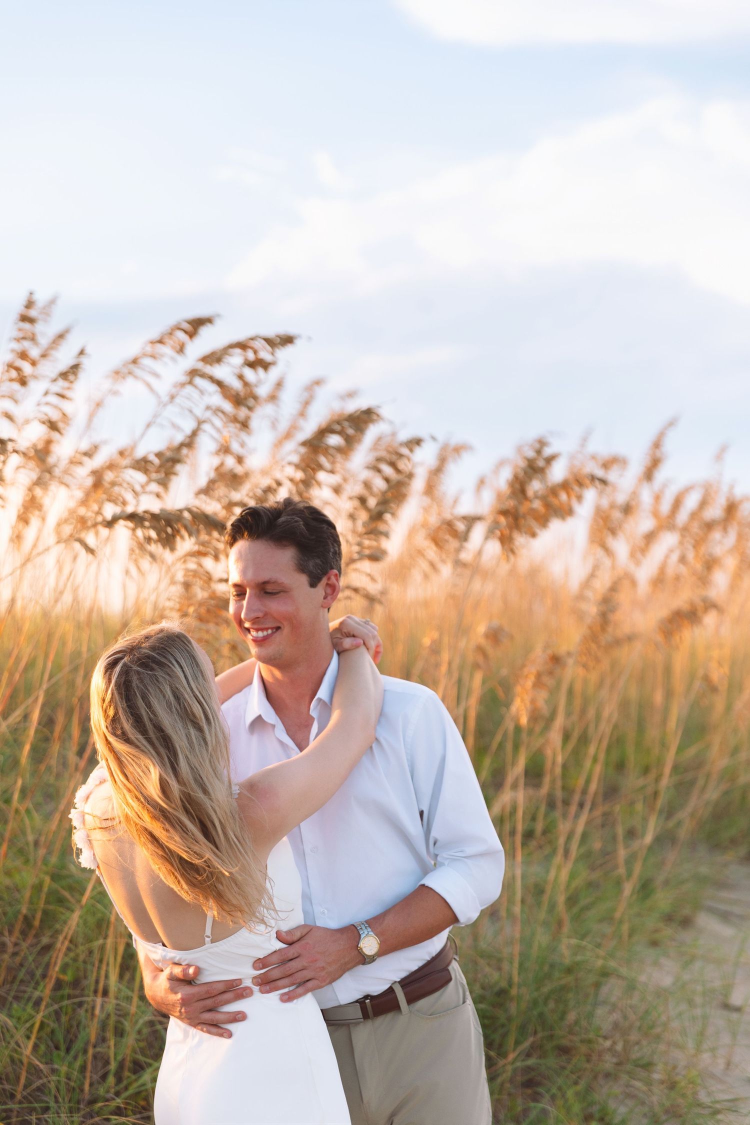 Happy couple embracing in golden sea oats at sunset on a beach.
