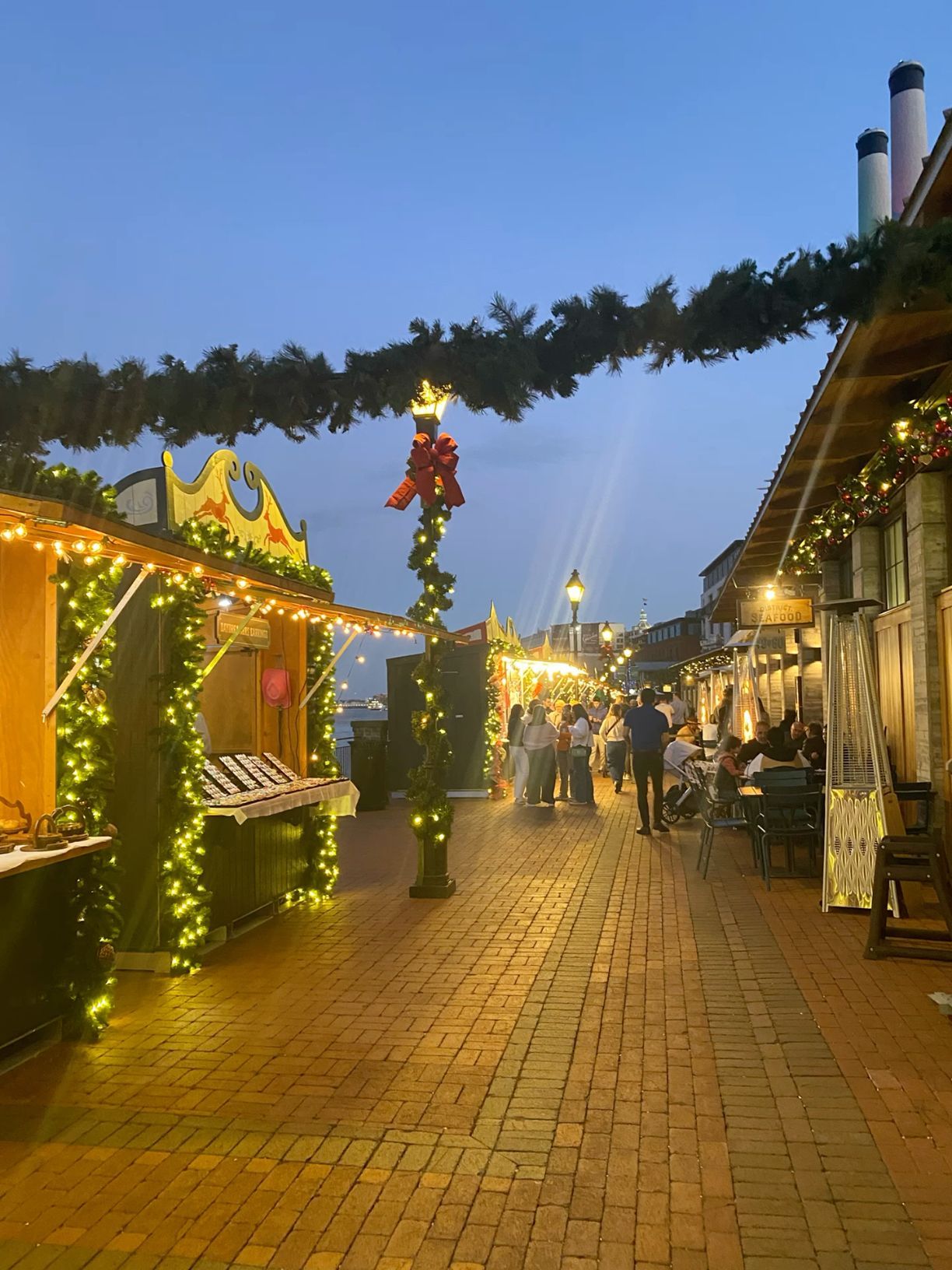 Festive Christmas market at dusk with string lights and holiday decorations.