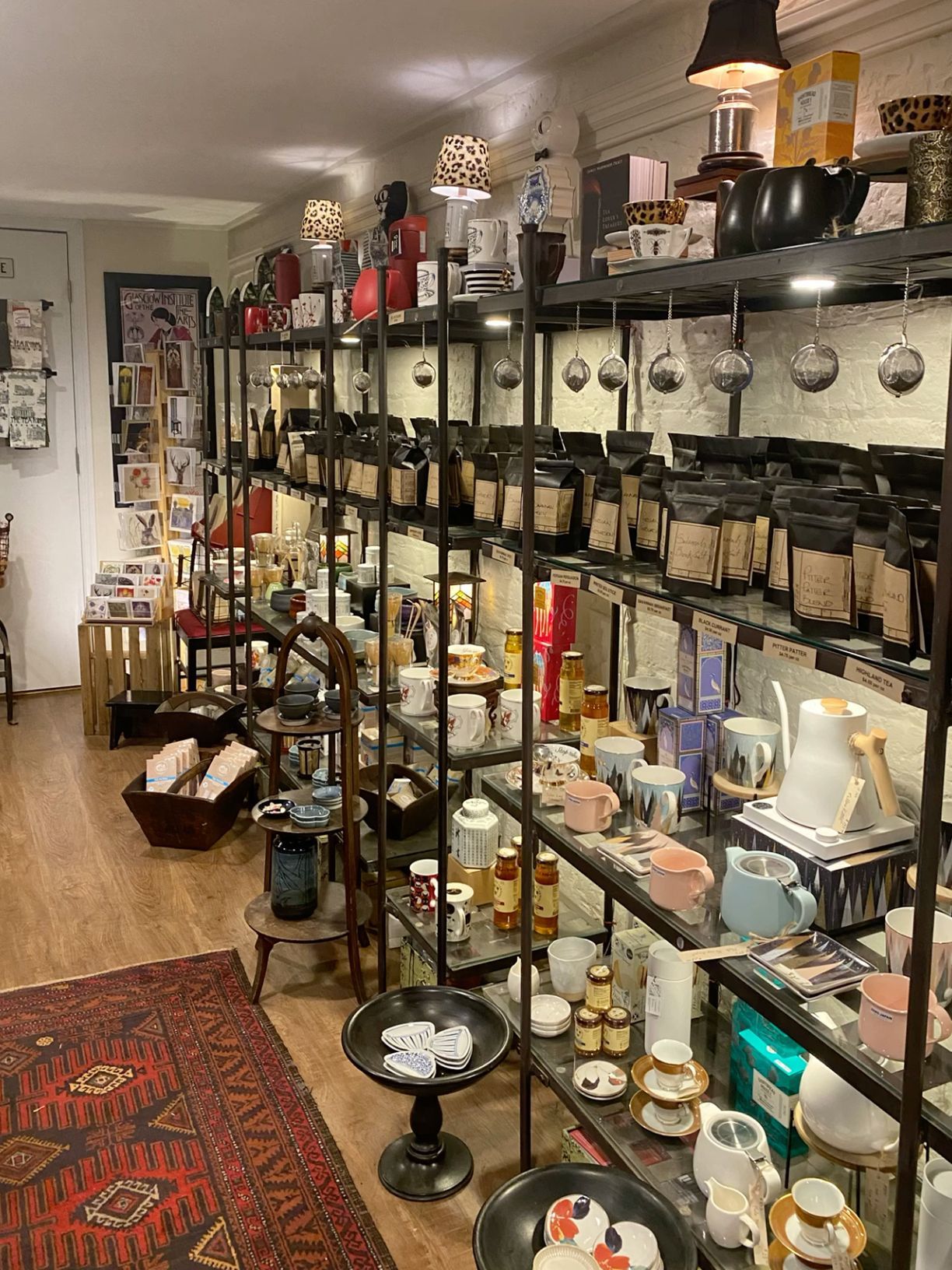Charming gift shop shelves stocked with teas, candles, ceramics, and home goods on black metal shelving.