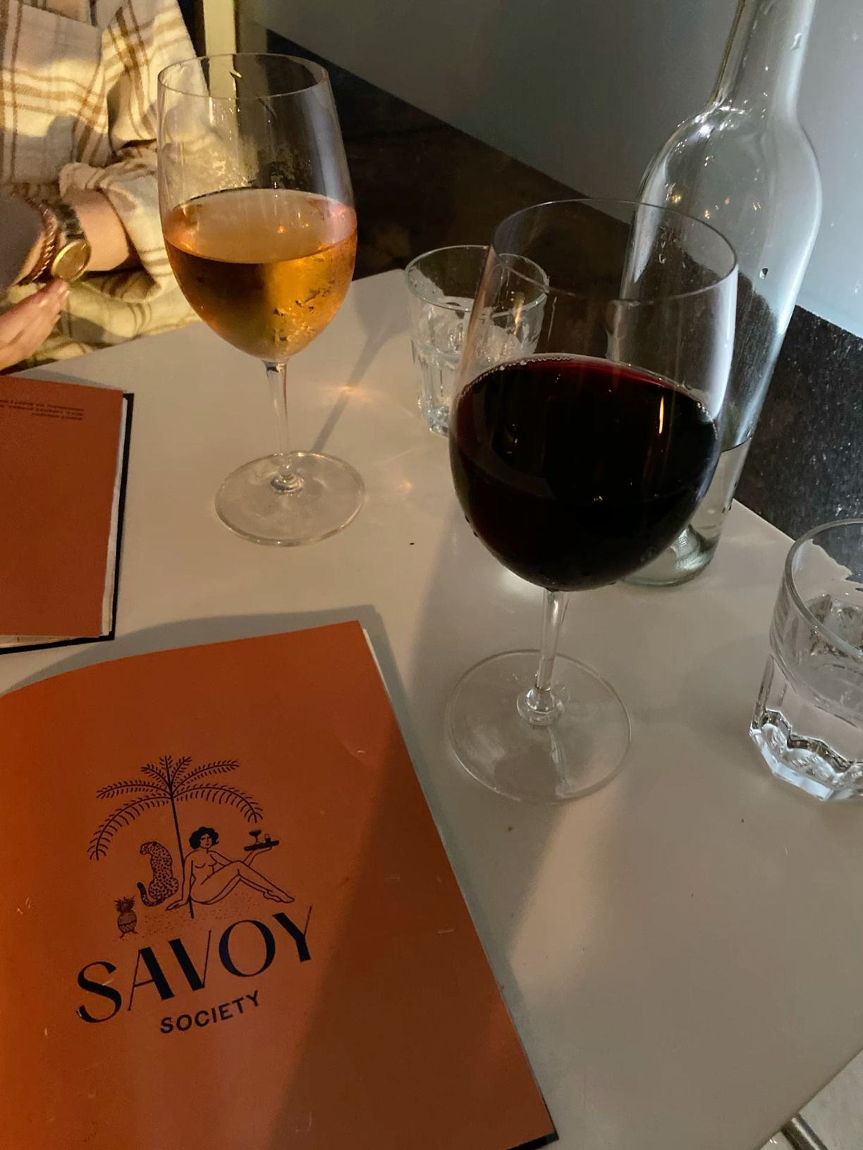 Savoy Society restaurant menu beside glasses of red and white wine on white table.