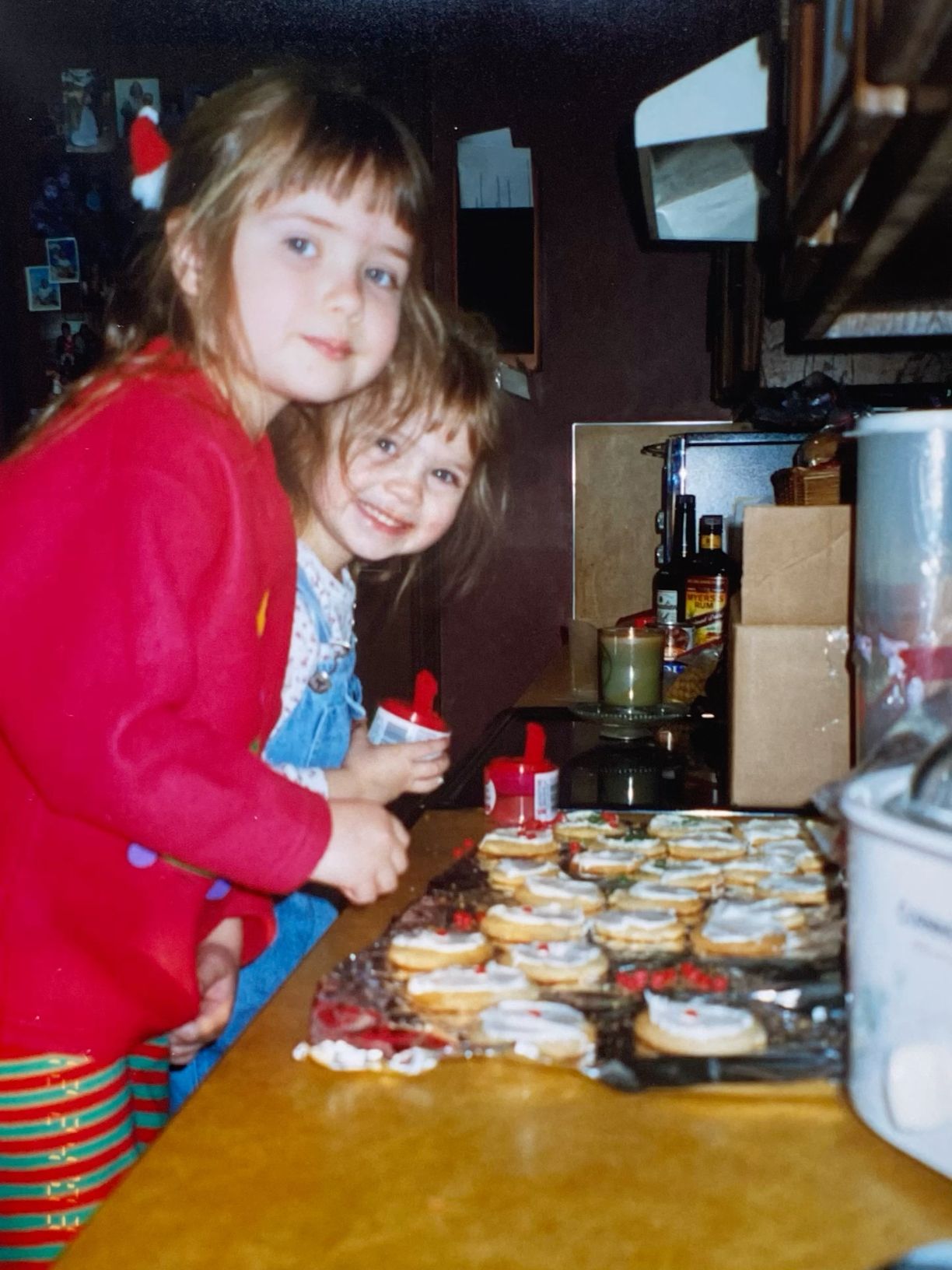 Two young sisters decorating Christmas cookies together on a baking sheet in a cozy kitchen.