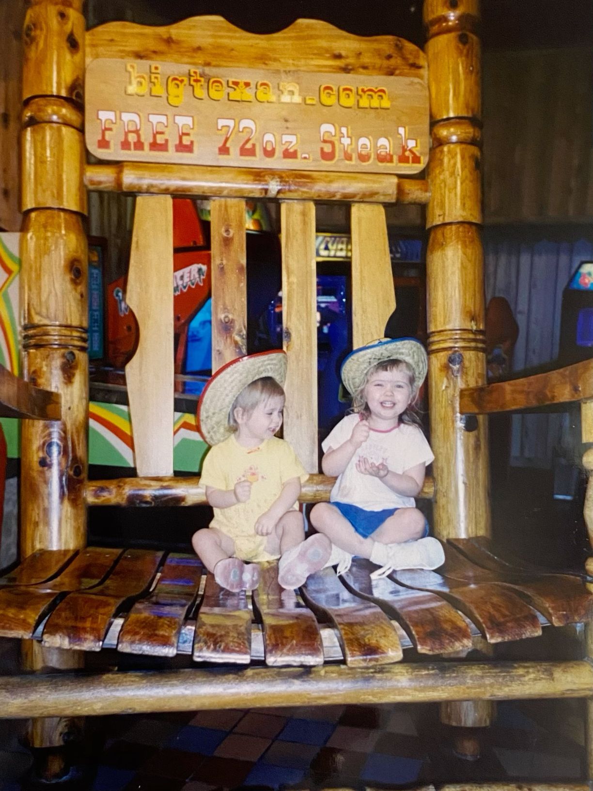 Two young children sitting in a giant wooden chair at a steakhouse restaurant.