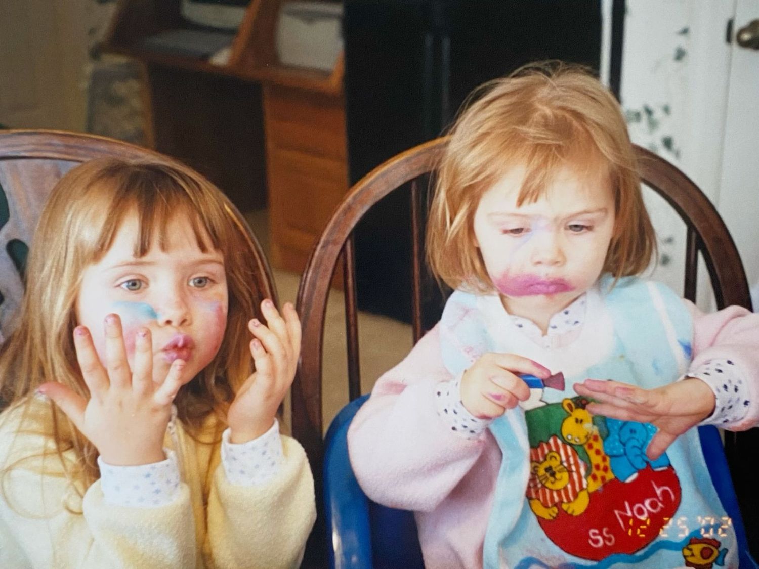Two young girls with messy faces sitting in wooden chairs, appearing to have been eating colorful food.