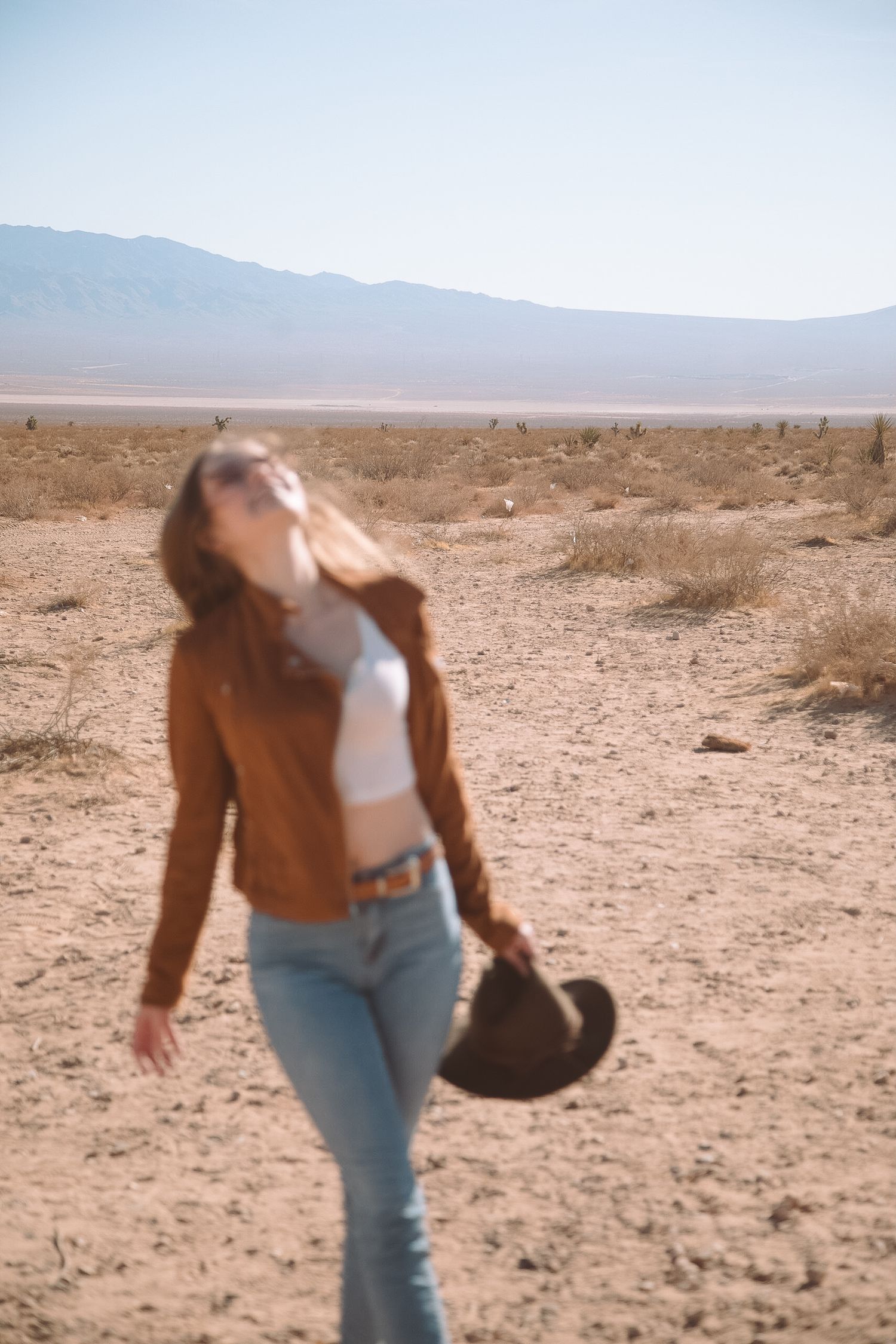Woman in brown jacket and jeans posing in a desert landscape.