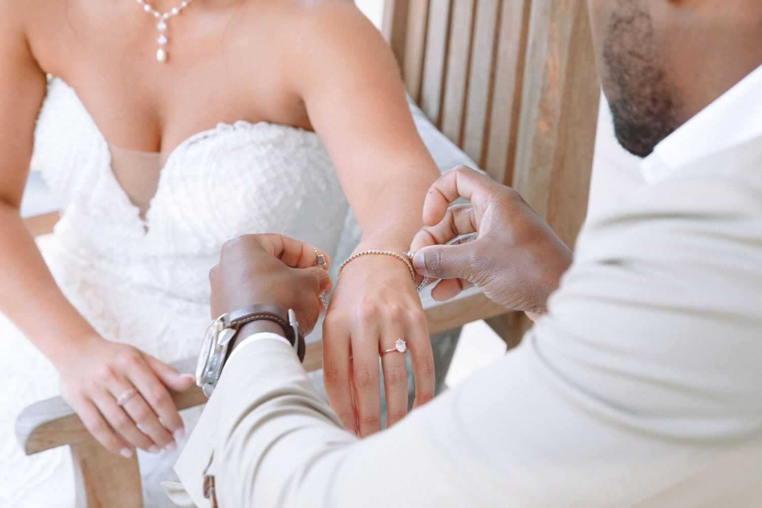 Groom fastening a bracelet on bride's wrist during wedding ceremony, close-up of hands with rings visible.