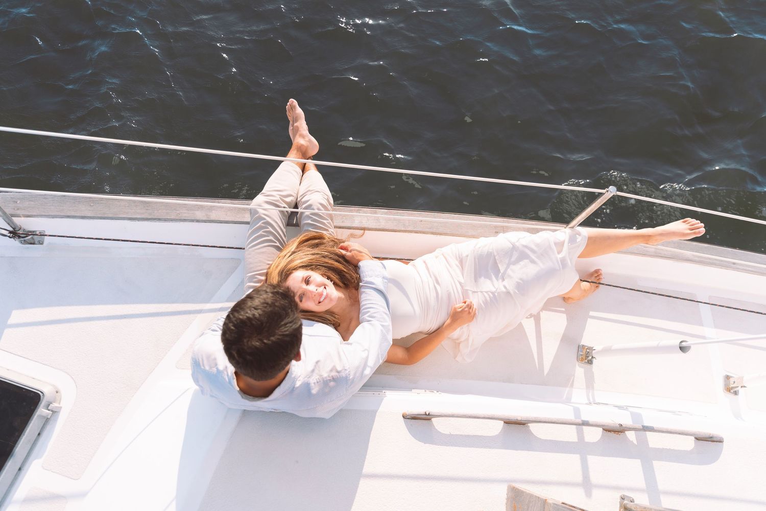 Romantic couple relaxing together on the deck of a white sailboat on calm blue water.
