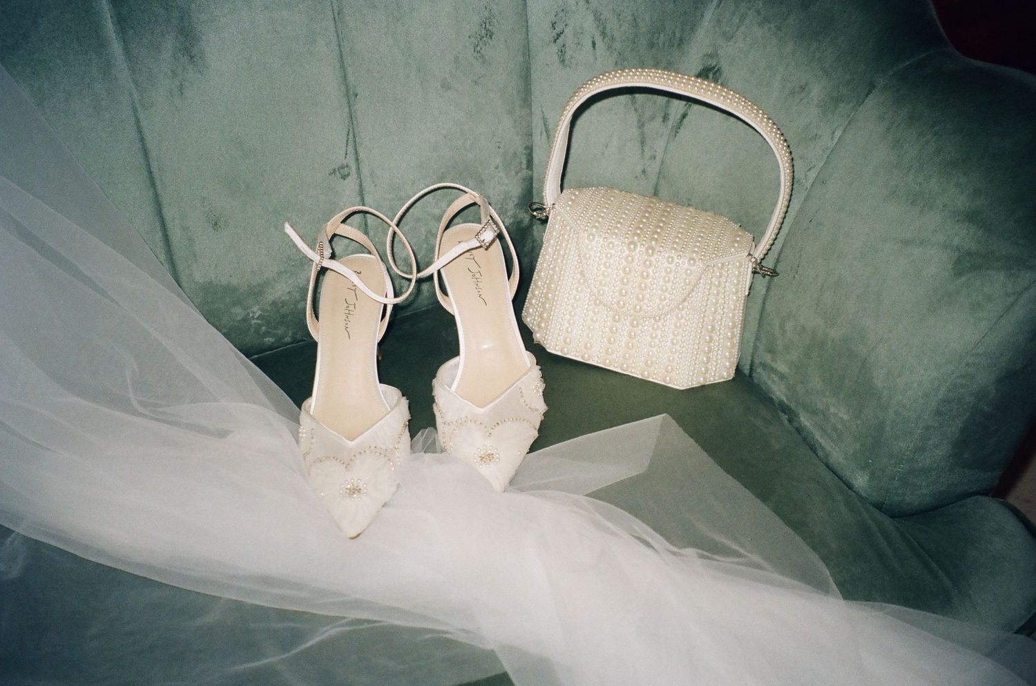 White bridal heels with bow detail and woven basket bag on gray surface with flowing tulle fabric.