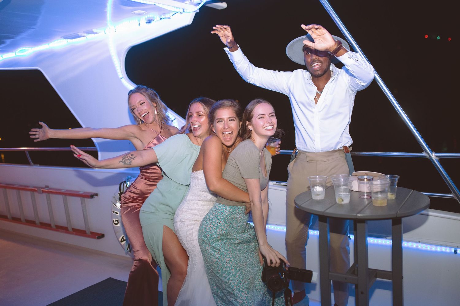 Group of friends celebrating and posing on a yacht deck at night during a party.