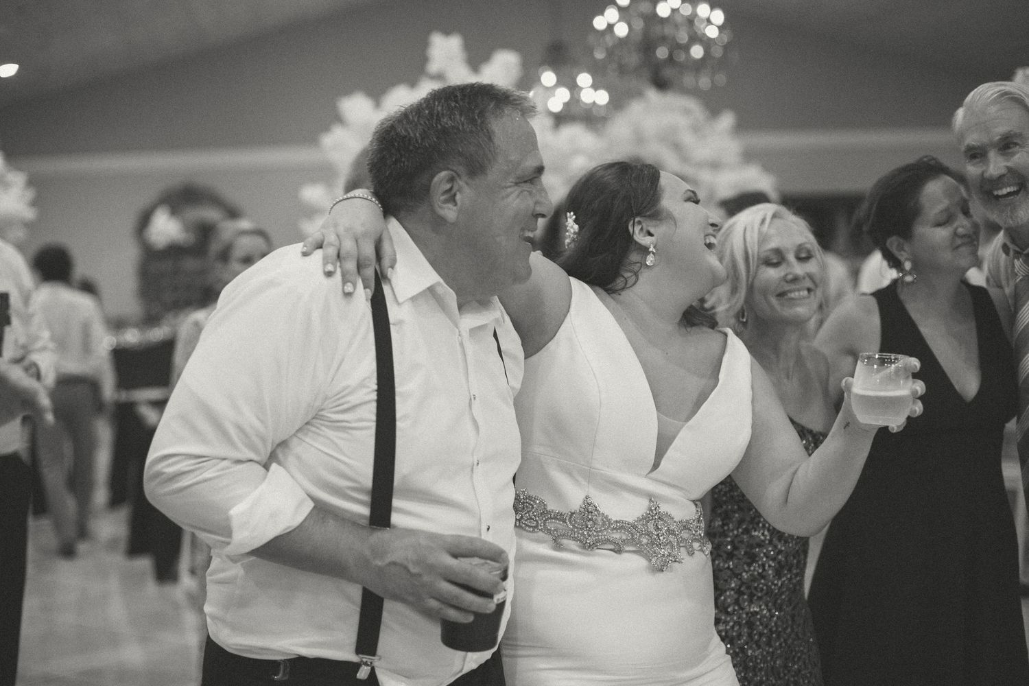 Bride and groom laughing joyfully with guests on the wedding reception dance floor.