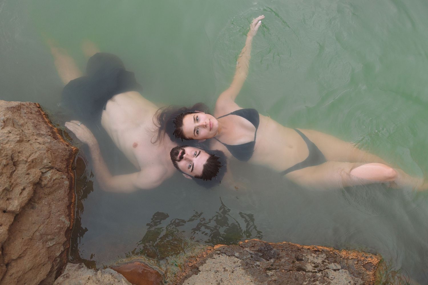 Top view of couple floating side by side in a green geothermal hot spring pool in Iceland.