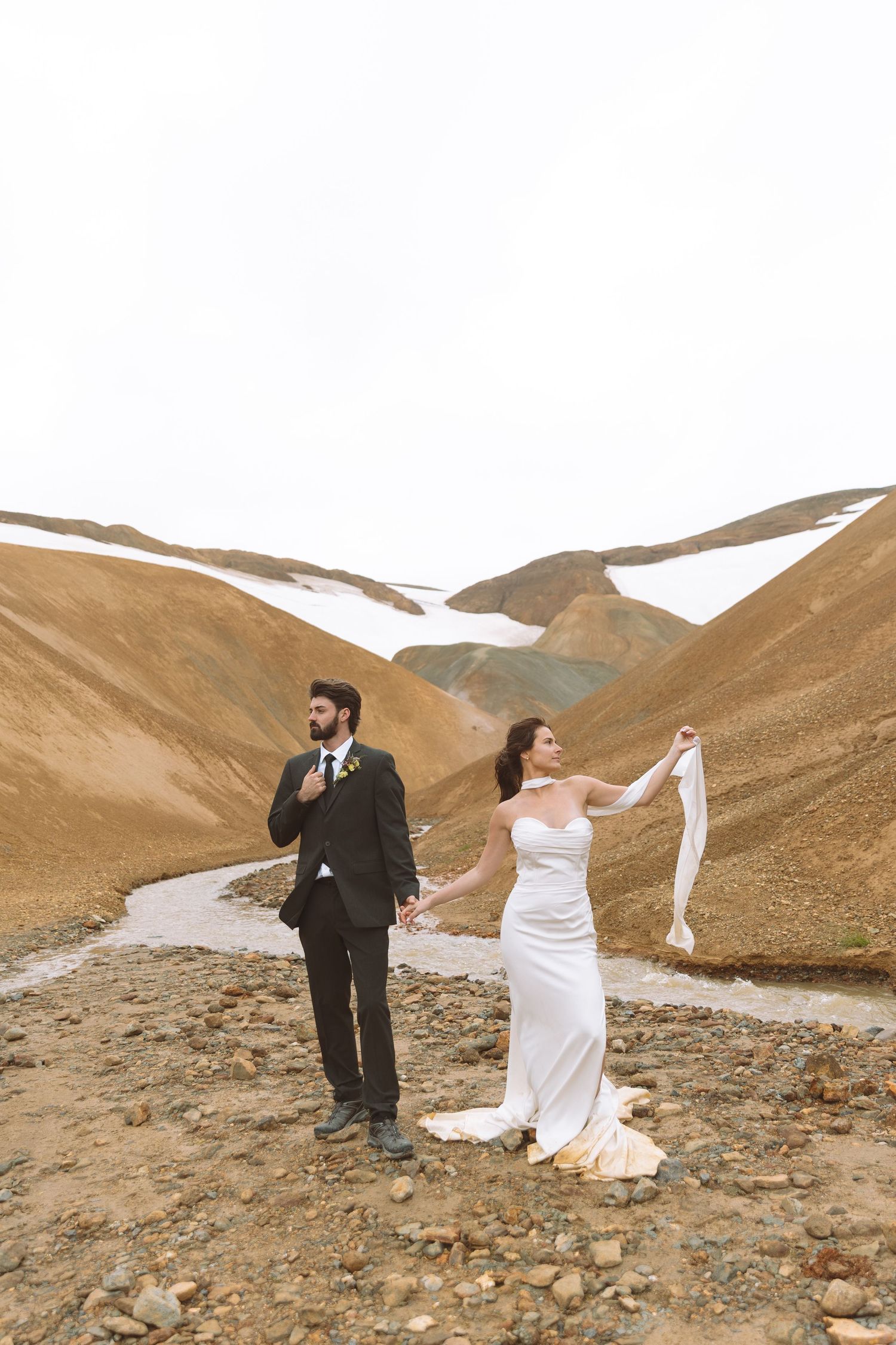 Bride and groom eloping in Iceland's dramatic highland landscape with snow-capped mountains.