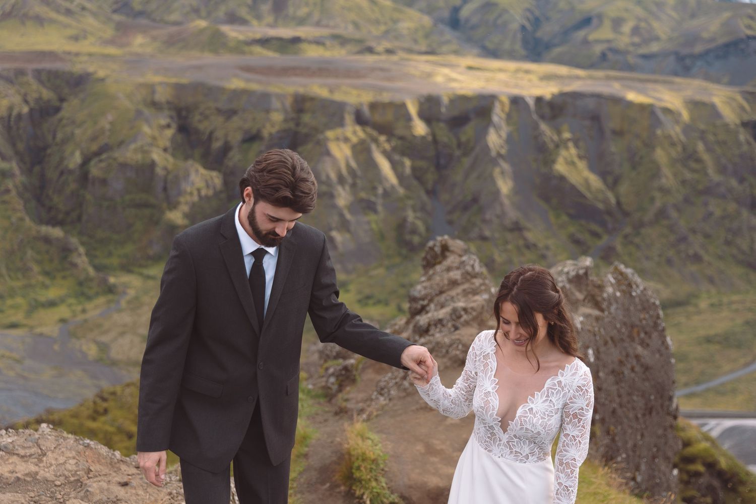 Groom tenderly holds bride's hand on a rugged Iceland cliffside during their romantic wedding elopement.