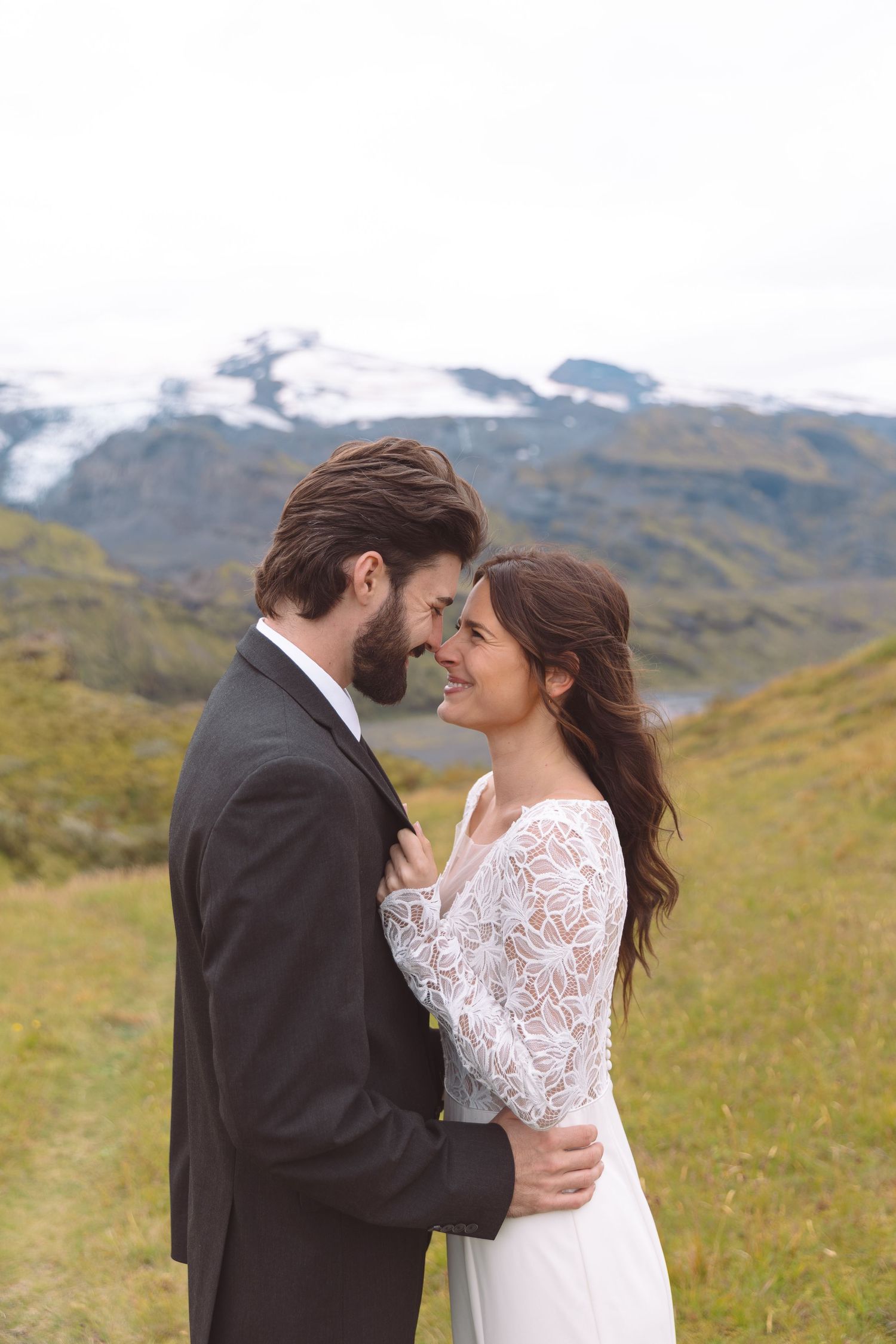 Smiling bride and groom gazing at each other lovingly with snow-capped Icelandic mountains in background.
