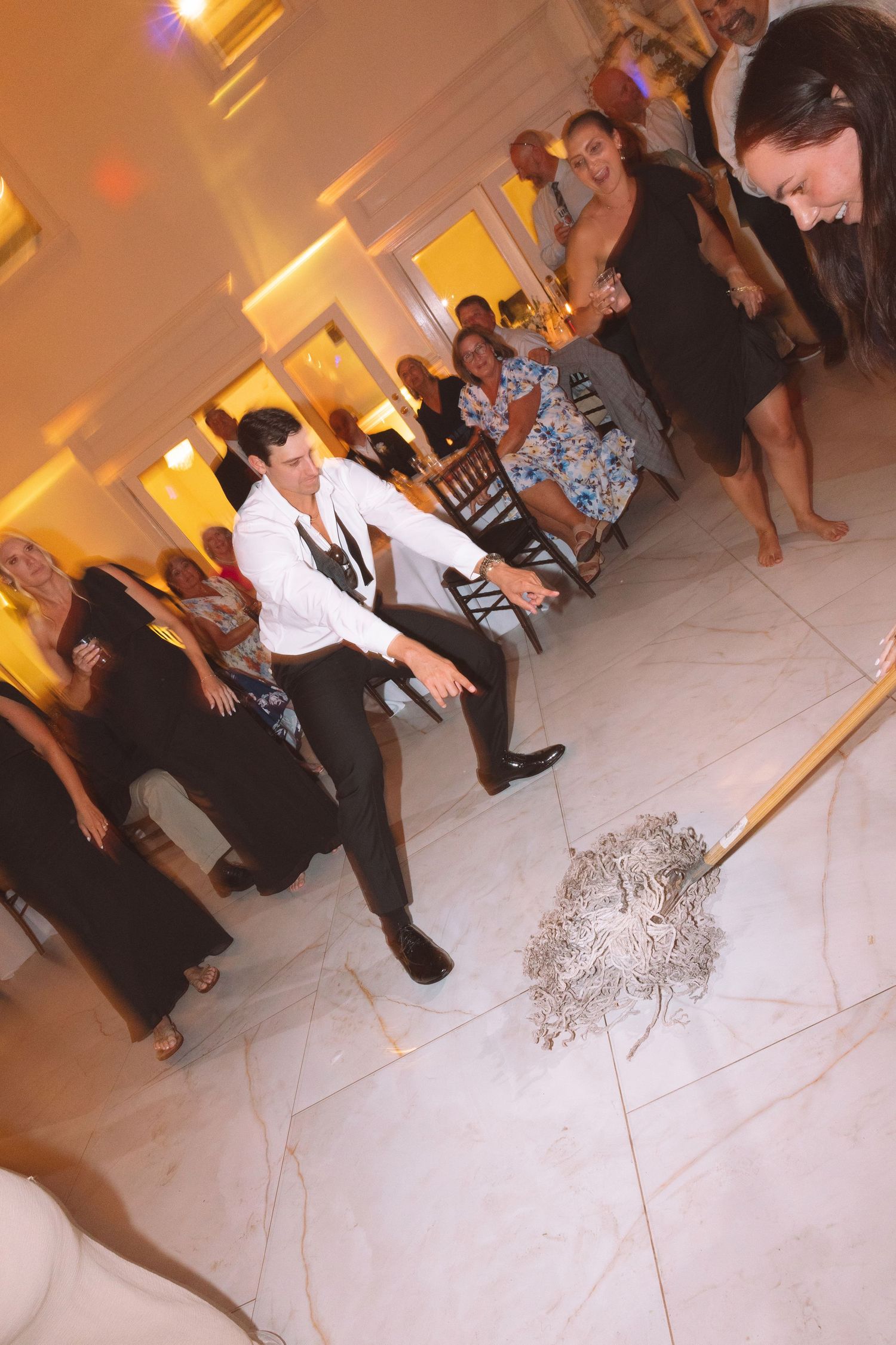 Wedding bouquet toss on marble dance floor with guests watching as bride throws flowers at reception.