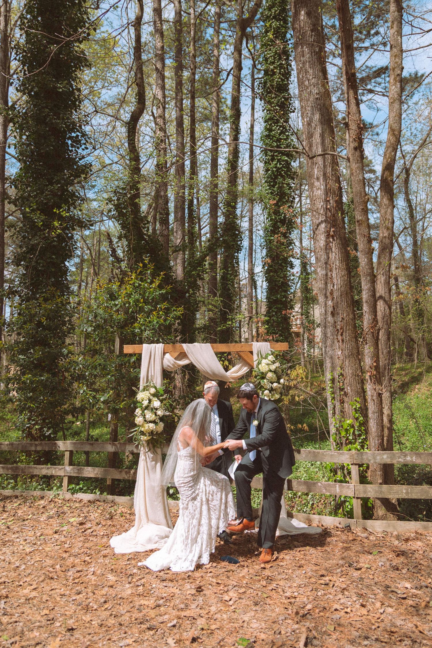 Bride and groom exchange vows at rustic outdoor woodland wedding ceremony with floral arch.