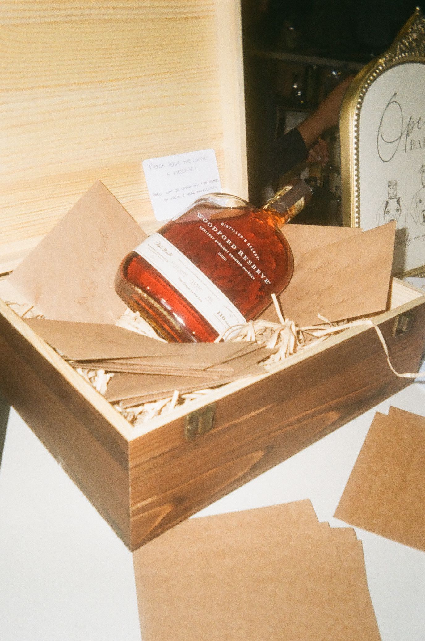 Woodford Reserve bourbon bottle in a rustic wooden gift box with straw packing and kraft paper cards.