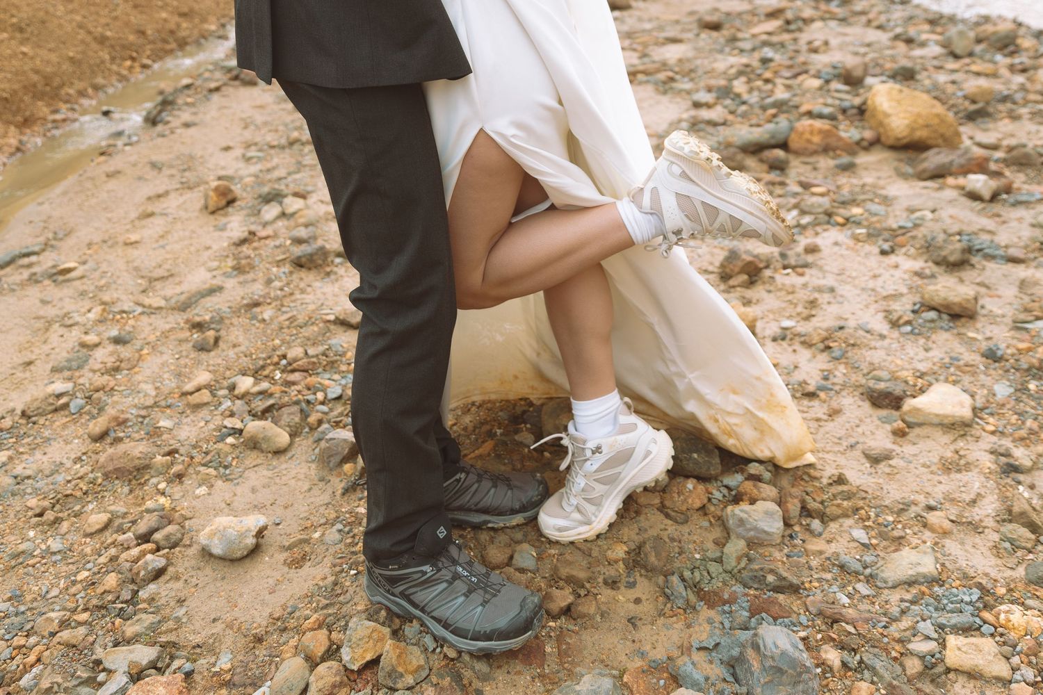 Close-up of bride in white sneakers and groom in hiking boots standing on rocky ground at their elopement.
