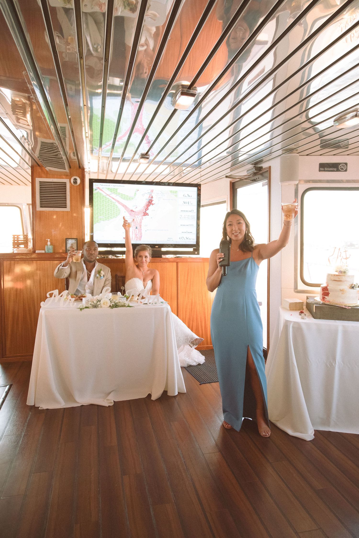 Bridesmaid in blue gown giving a toast at a boat wedding reception while the couple sits at their sweetheart table.
