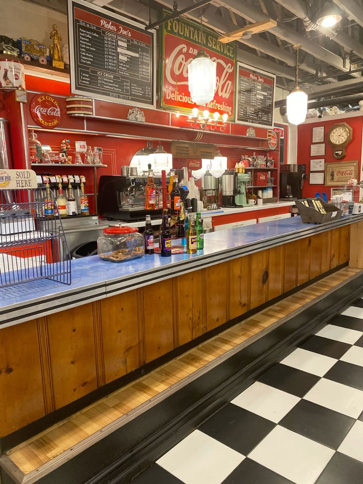 Vintage retro soda fountain counter with Coca-Cola signs and black white checkered floor.