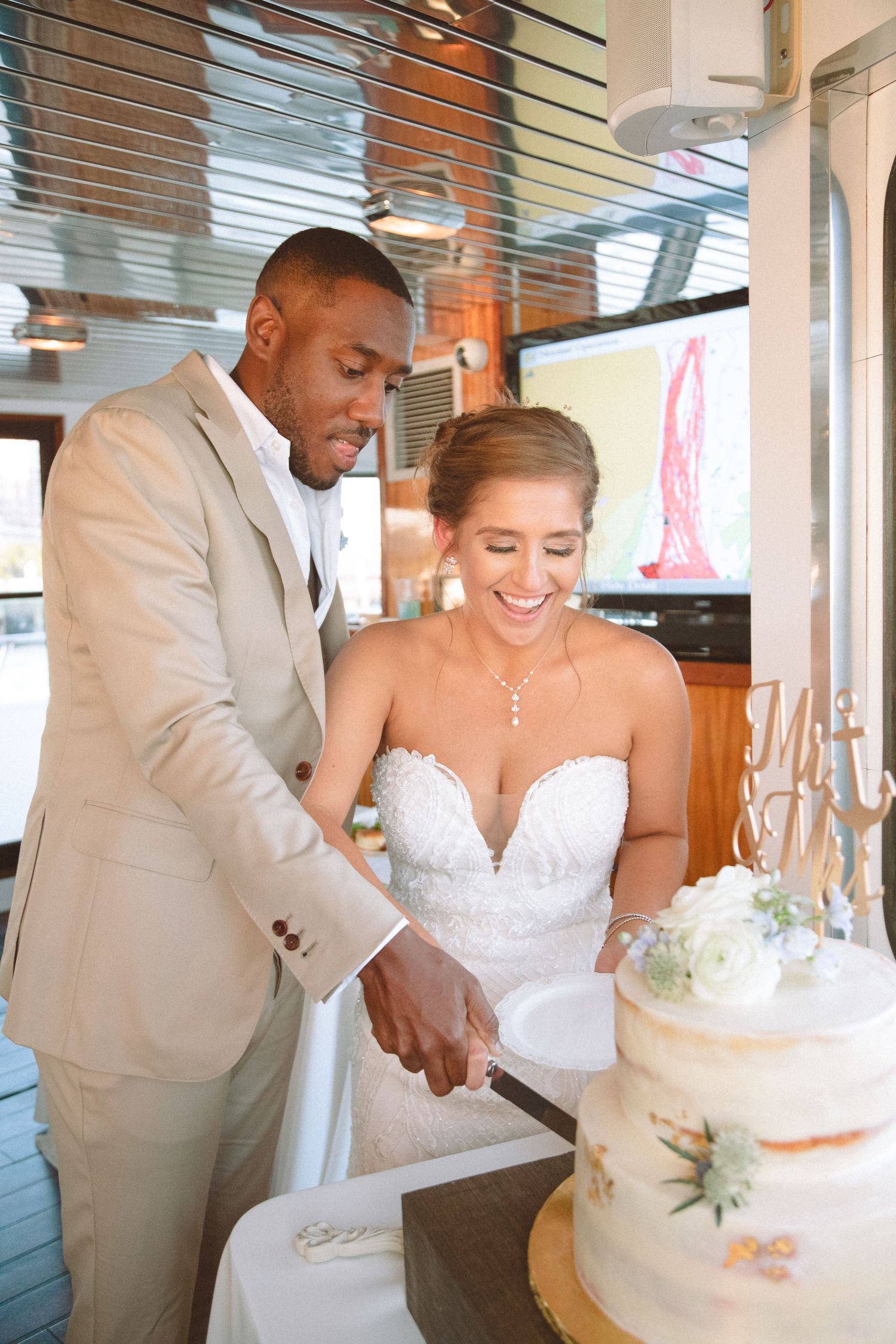 Bride and groom cutting their two-tier wedding cake together aboard a boat reception venue.