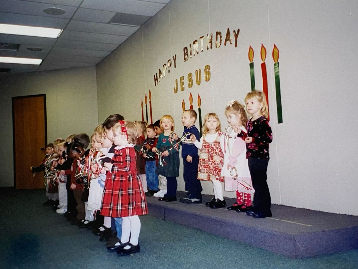 Young children line up on a stage beneath a Happy Birthday Jesus sign holding candles.