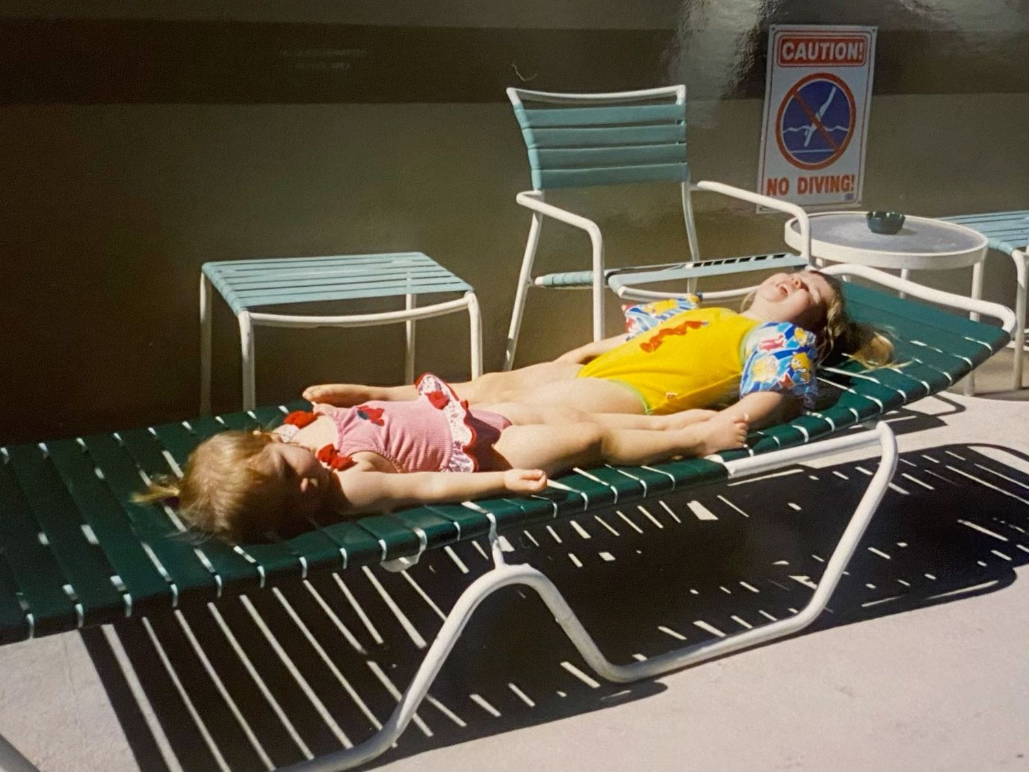 Two young children relaxing on lounge chairs by a pool in summer.