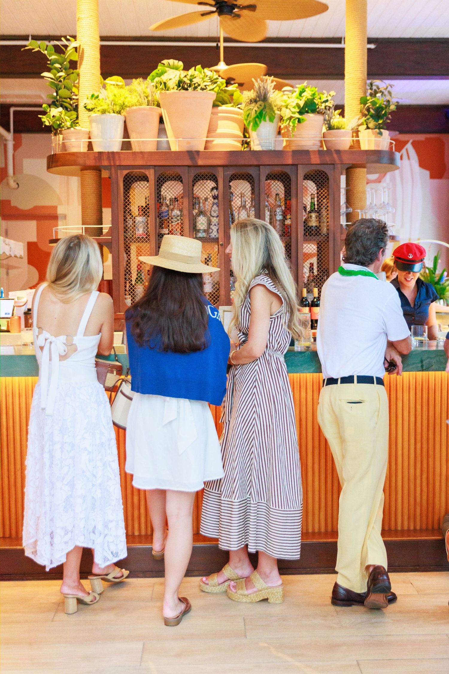 Four guests standing at a tropical bar with lush greenery and warm wood decor at an elegant event.