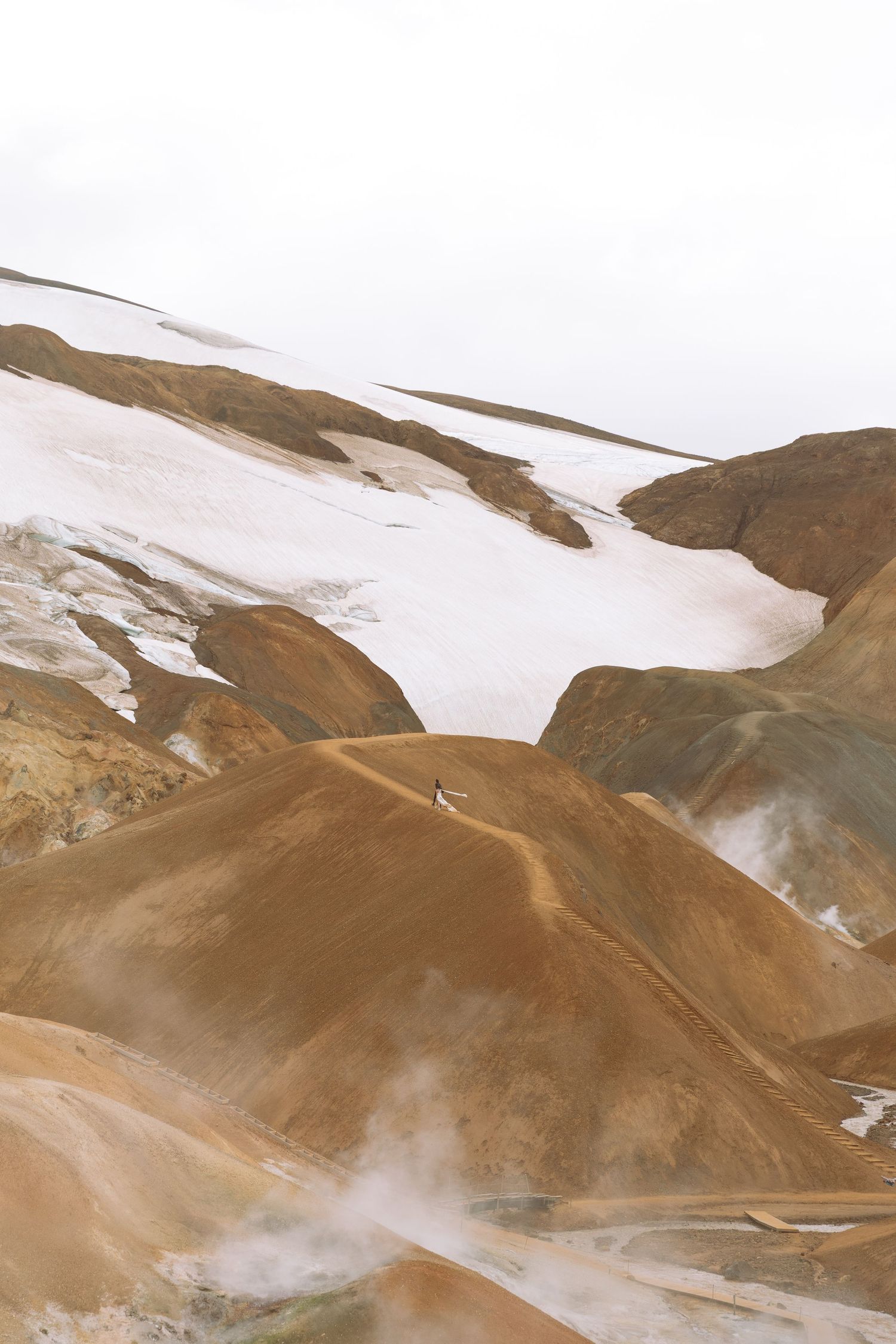 Geothermal steam rising over colorful rhyolite mountains with snow in Iceland's highlands.
