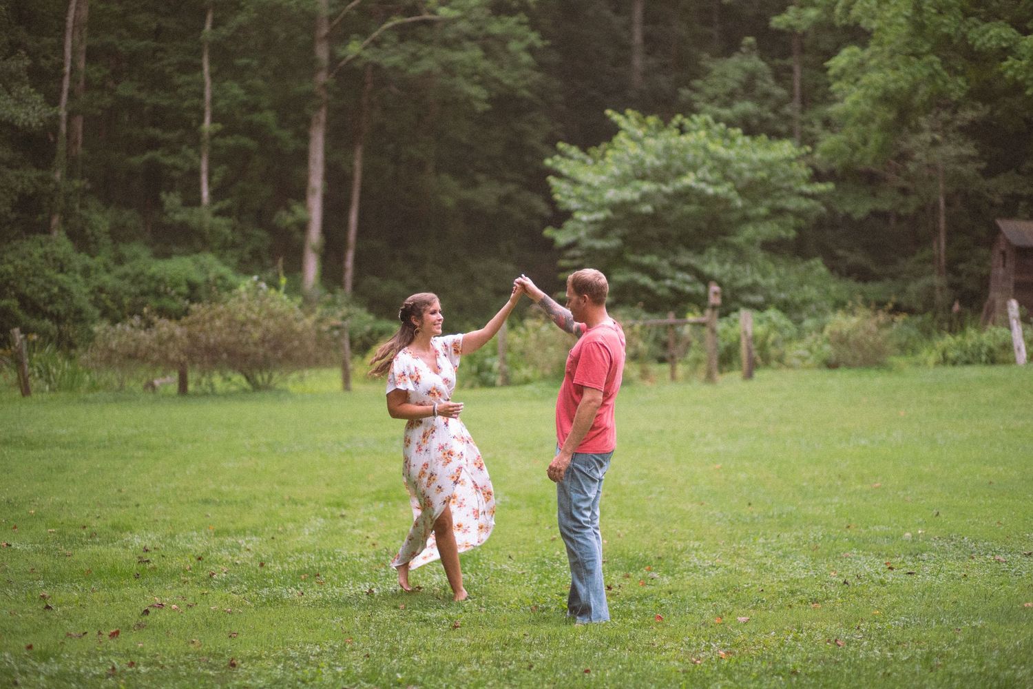 Joyful couple dancing and spinning together in a green meadow surrounded by trees.