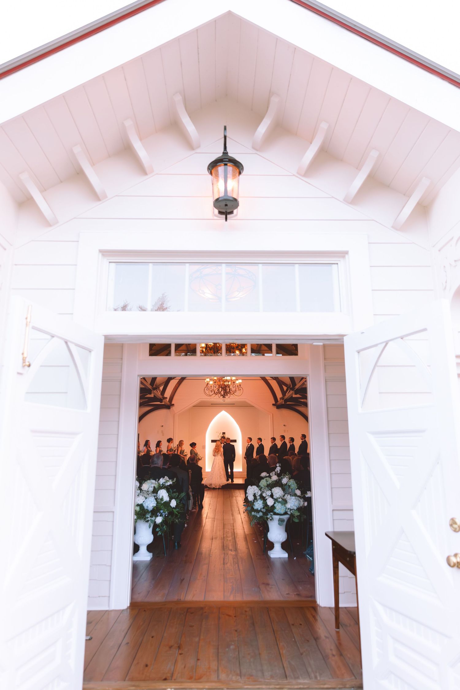 Elegant white chapel wedding venue entrance with open barn doors revealing guests seated inside.