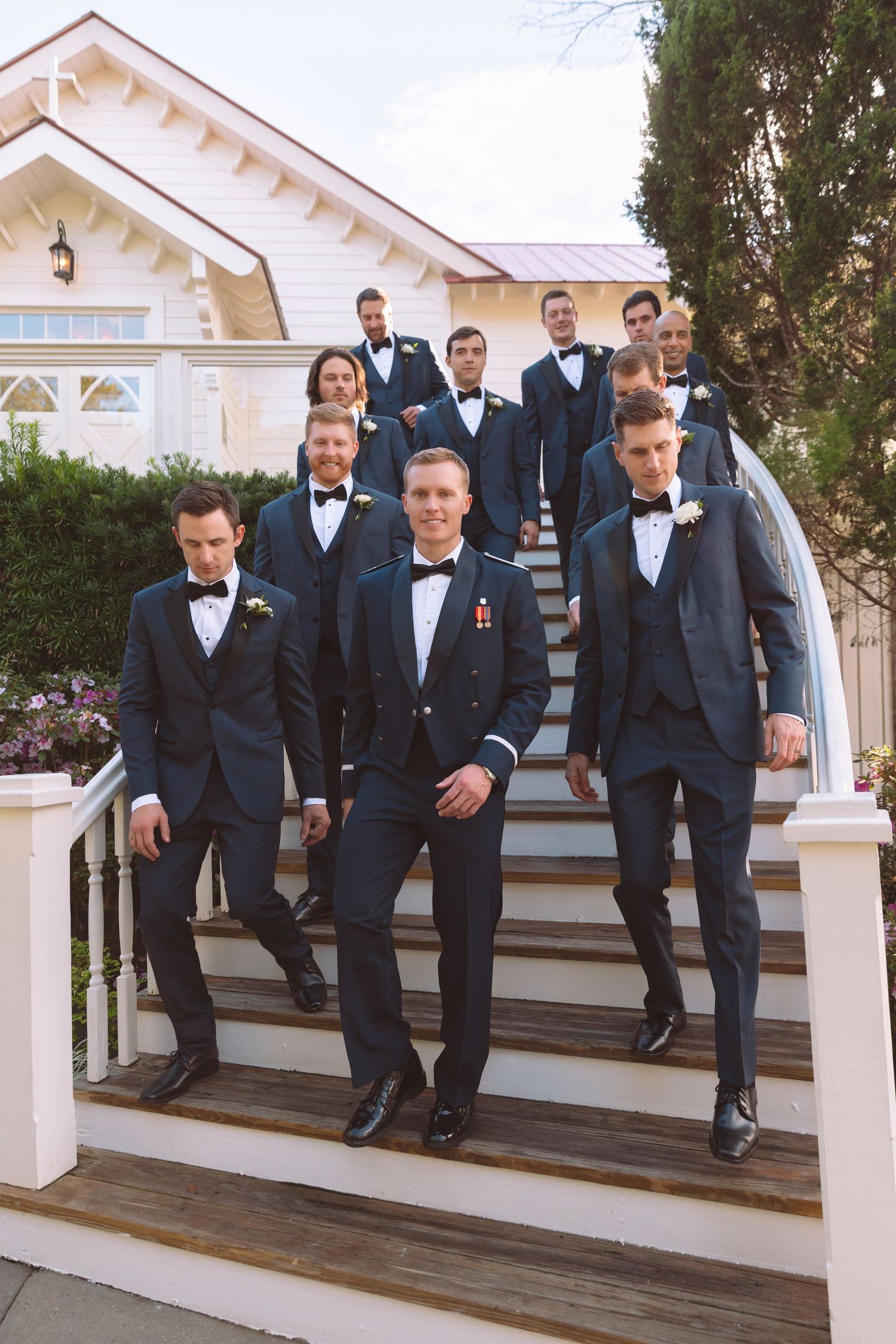 Groomsmen in navy tuxedos descending outdoor staircase at elegant wedding venue in a coordinated group photo.