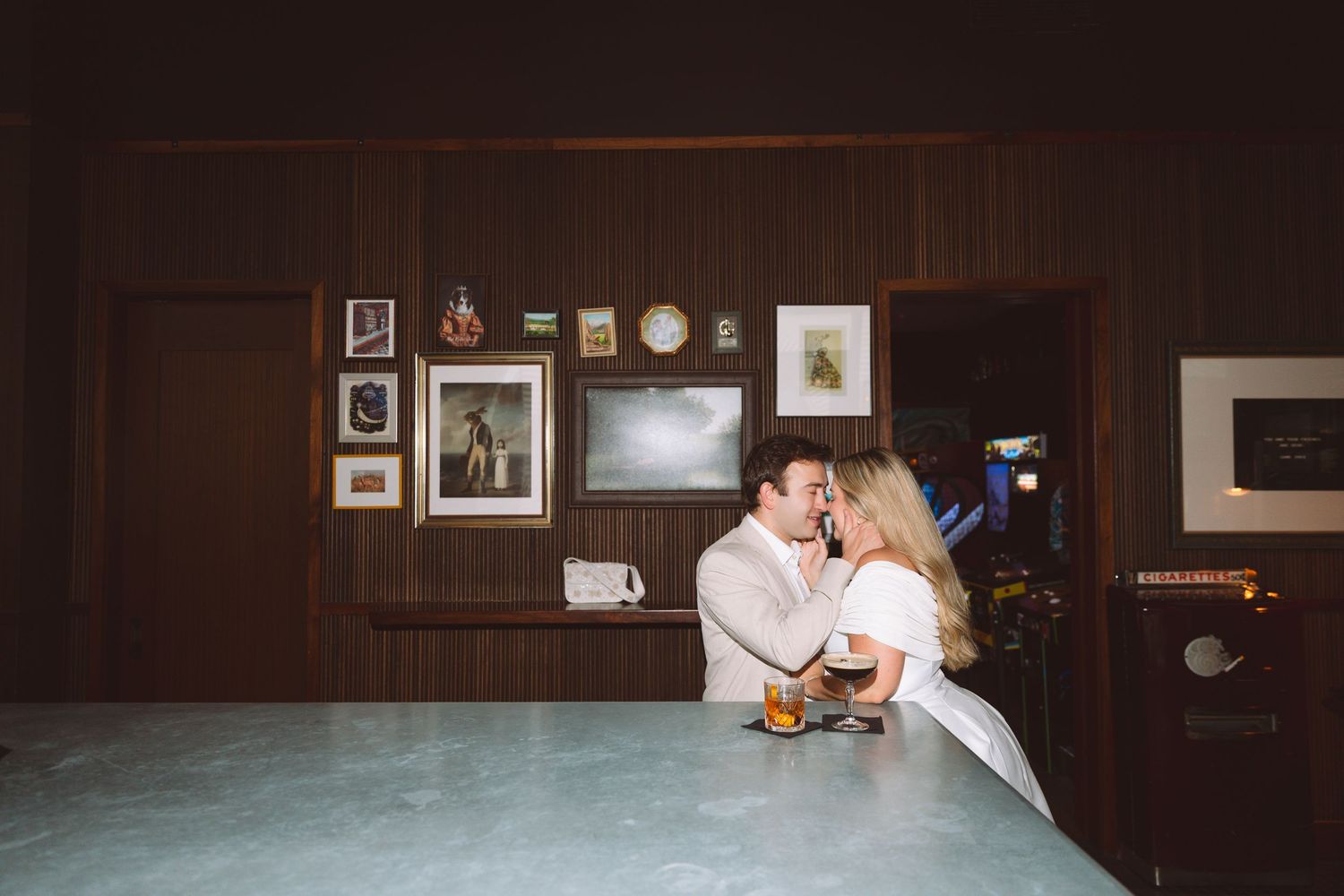 Couple sharing a romantic moment at a vintage bar with wood-paneled walls and framed artwork in the background.